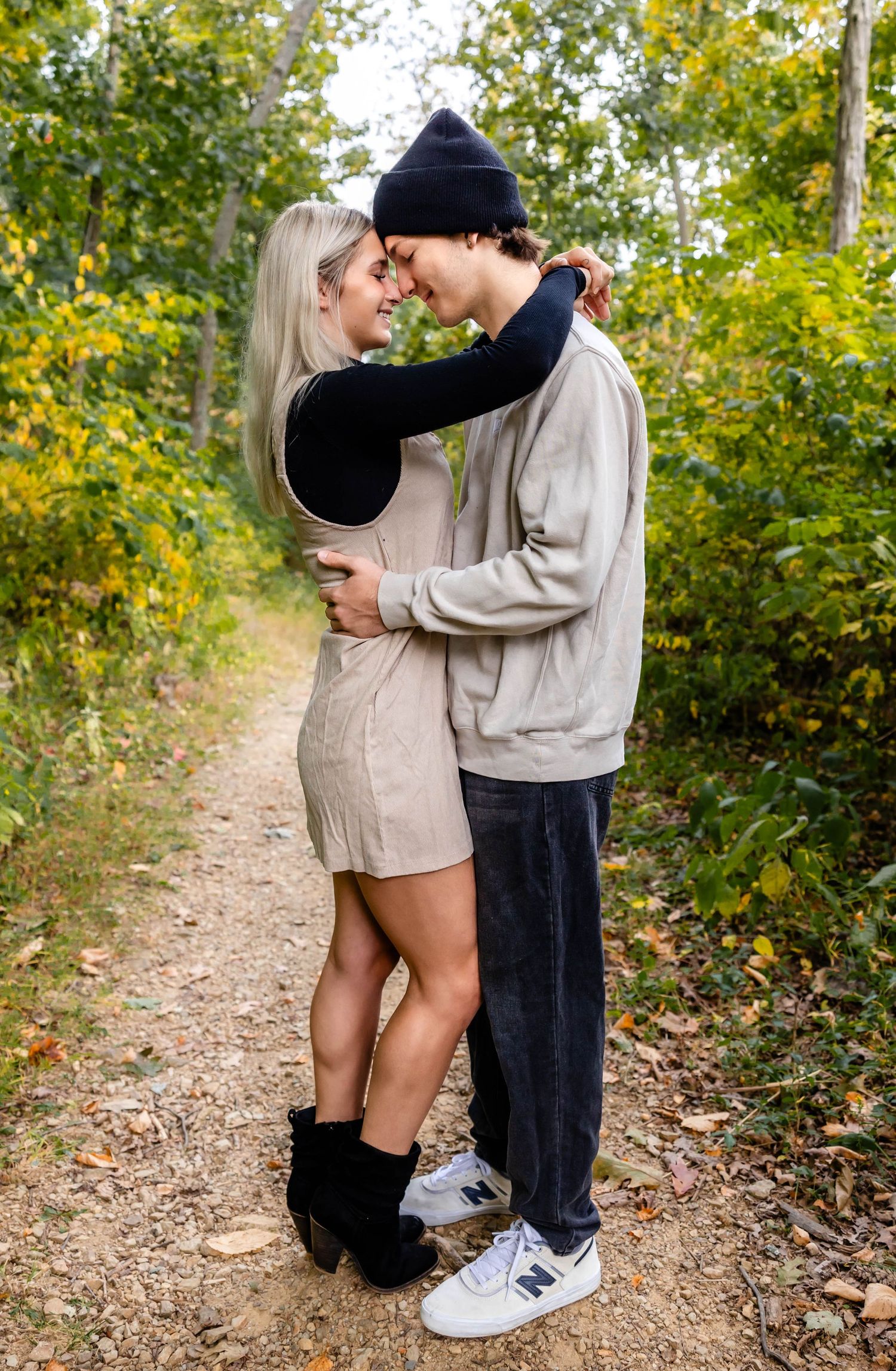 A couple shares a tender embrace on a wooded trail surrounded by fall colors.