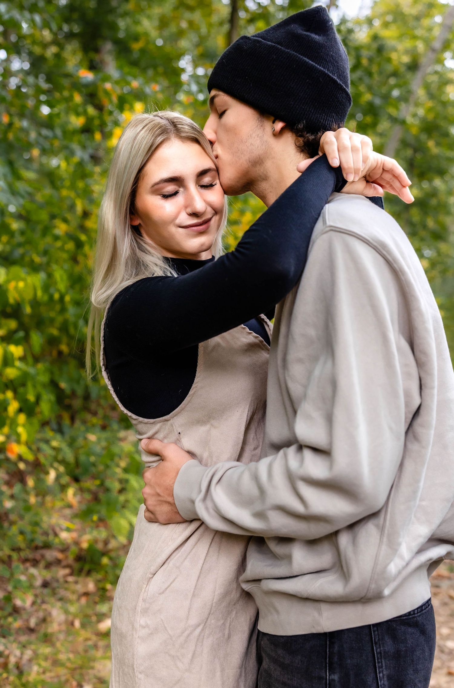 A tender moment between a couple on a nature trail with autumn leaves in the background.