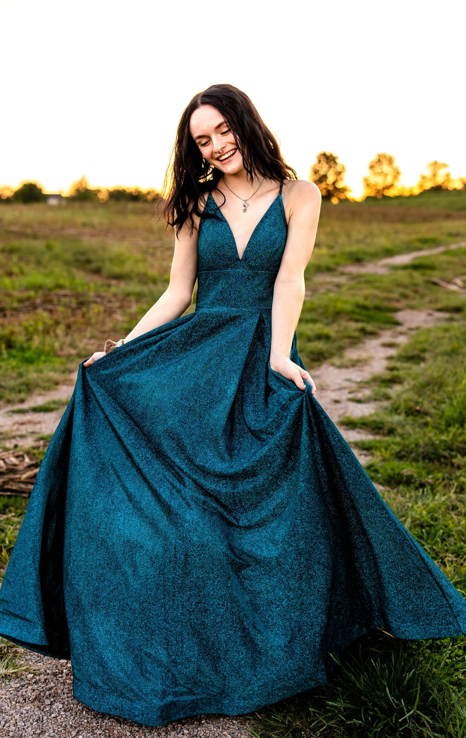 Elegant teal ballgown sparkles during outdoor sunset photoshoot on rustic path.