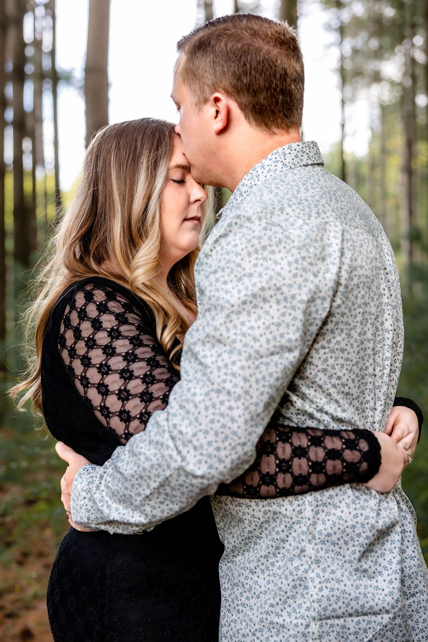 Tender embrace between couple surrounded by towering pine trees during photo session.