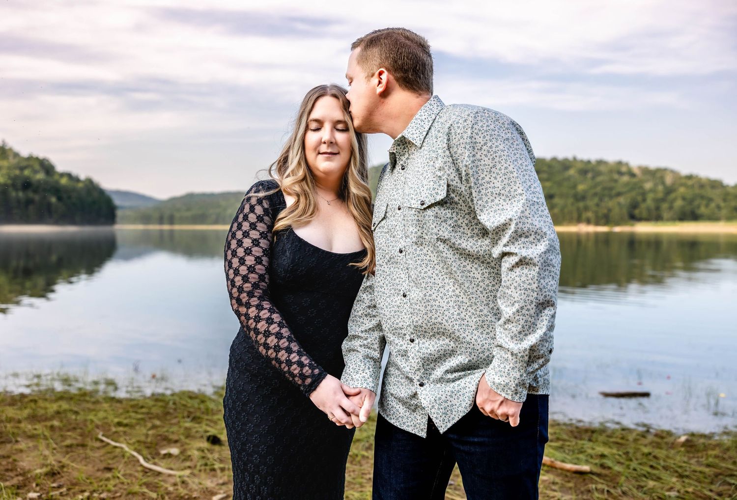 A romantic lakeside moment between a couple wearing casual attire against a scenic backdrop.