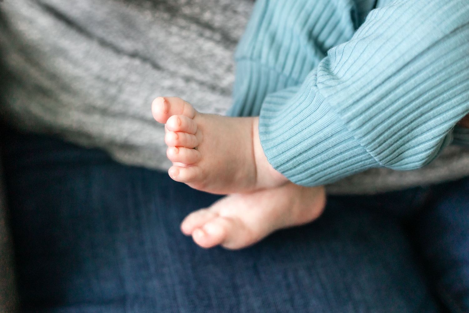 Close-up of tiny bare baby feet in soft blue clothing.
