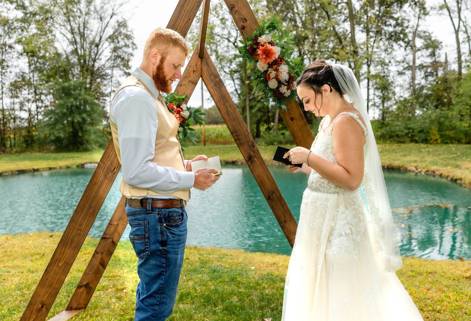 Emotional exchange of vows during an outdoor wedding ceremony under a wooden triangle arch.