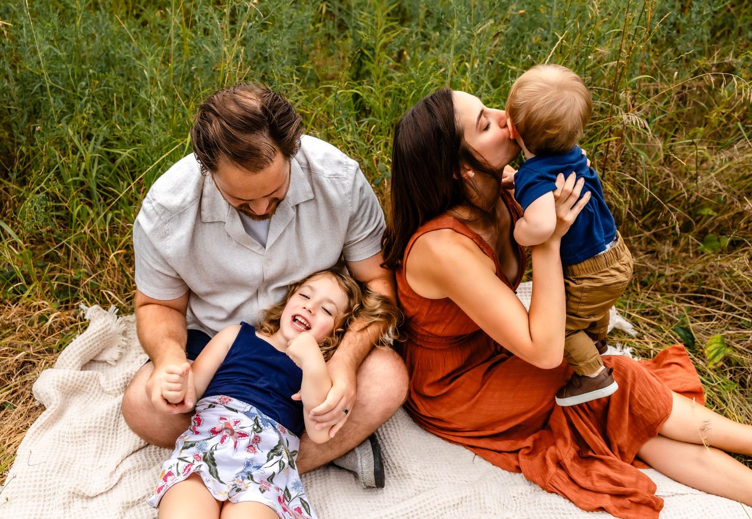 Playful family portrait on a blanket showing affectionate moments and genuine smiles.