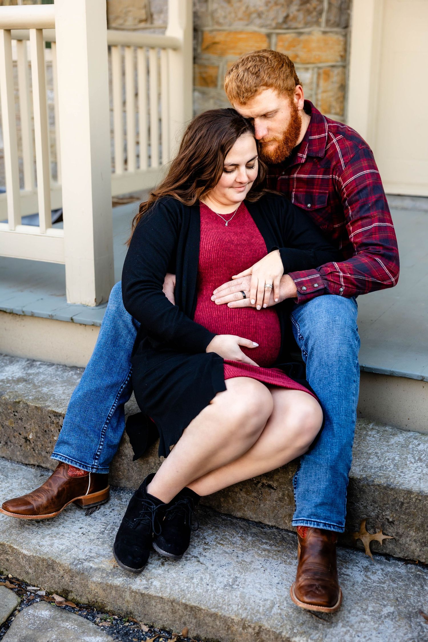 A couple shares an intimate moment while sitting on stone steps during a maternity photo session.