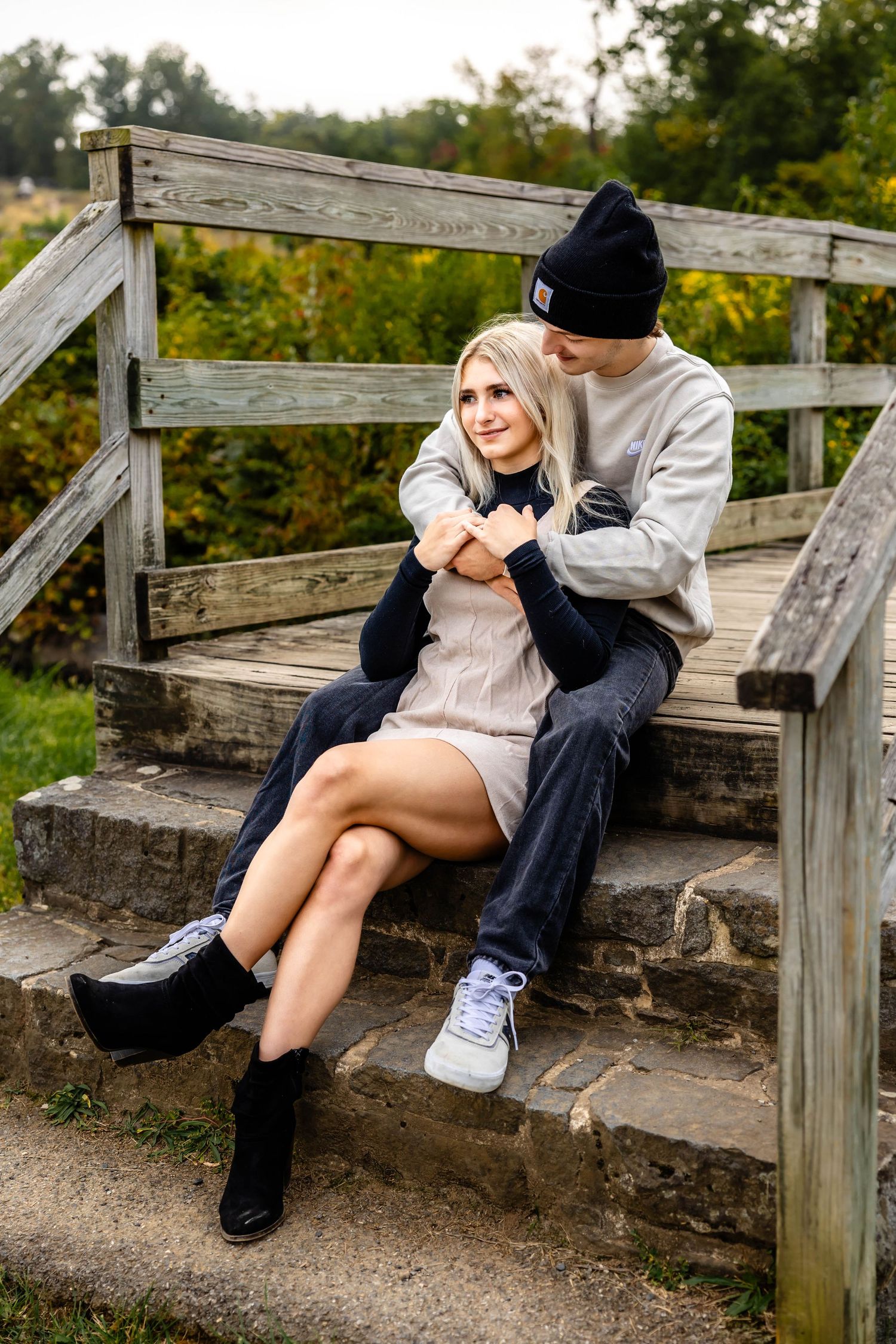 A couple embraces while sitting on wooden stairs in nature.