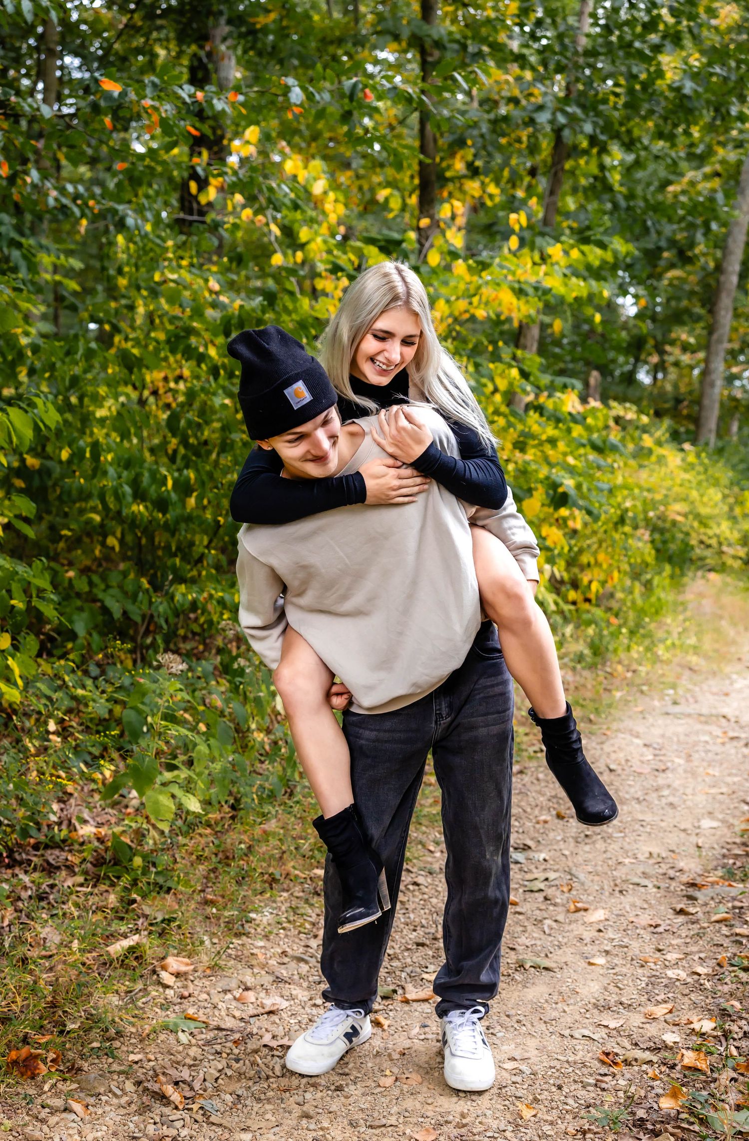 A joyful couple sharing a piggyback ride moment on an autumn forest path.