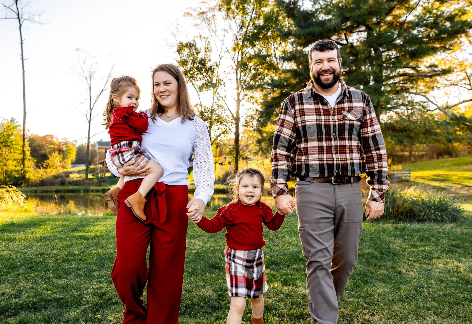 Family enjoying outdoor autumn photoshoot in coordinated red and plaid outfits.