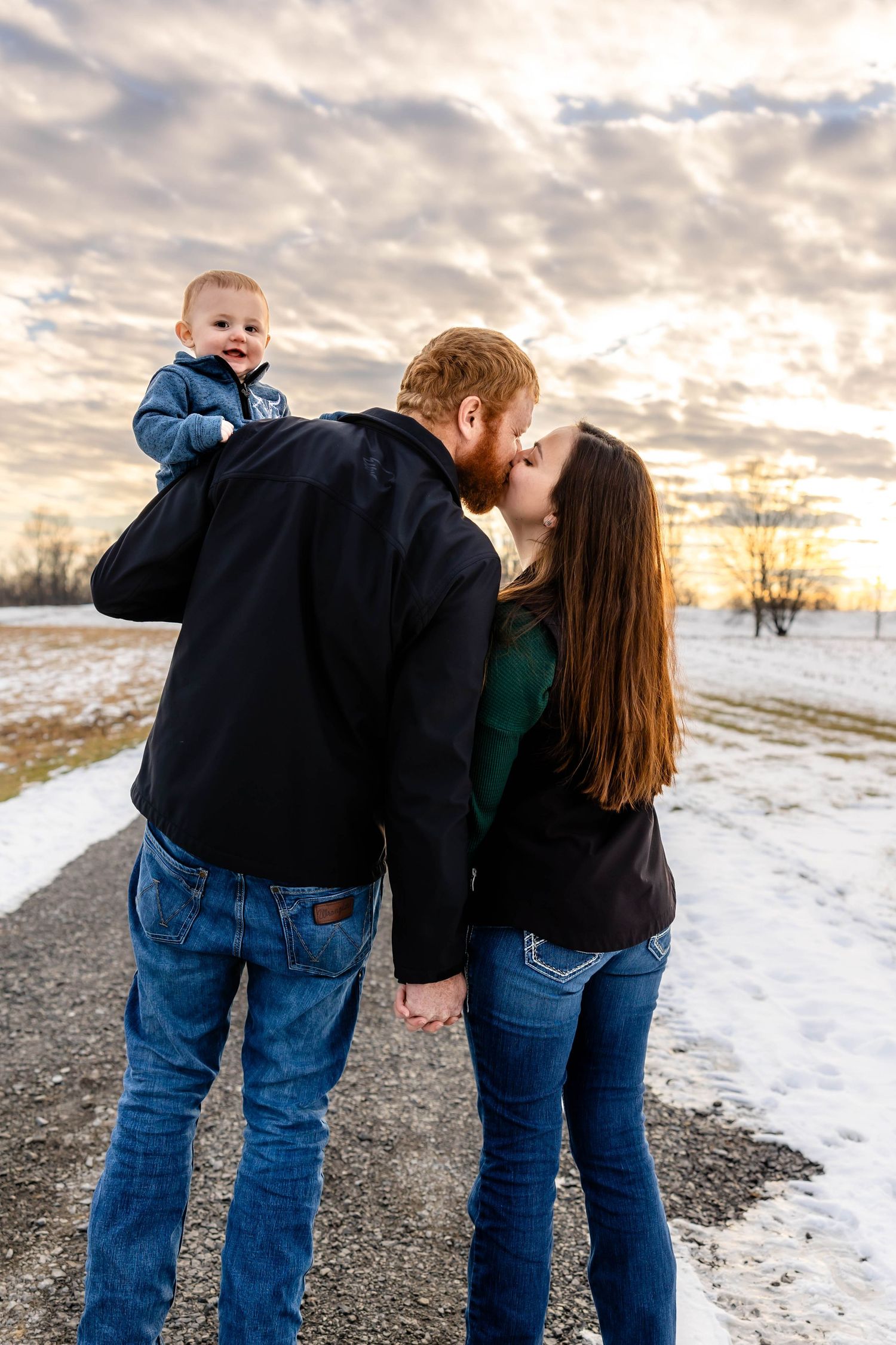 Family shares loving embrace on winter path at sunset.