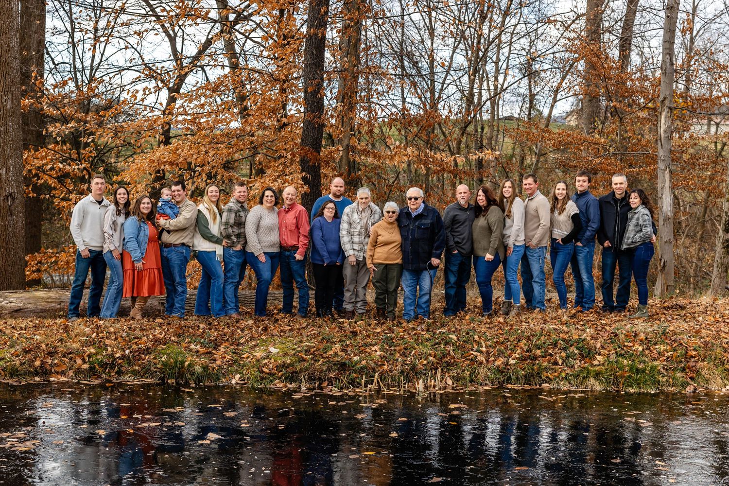 Large group photo of extended family gathered by waterfront during fall season.