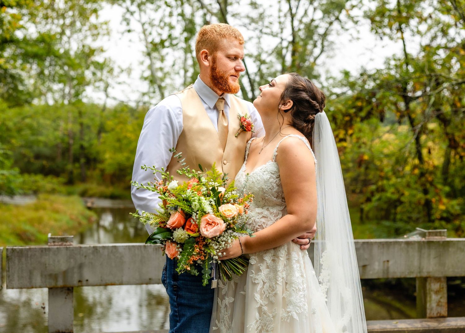 Romantic wedding portrait with colorful bouquet on rustic wooden bridge.