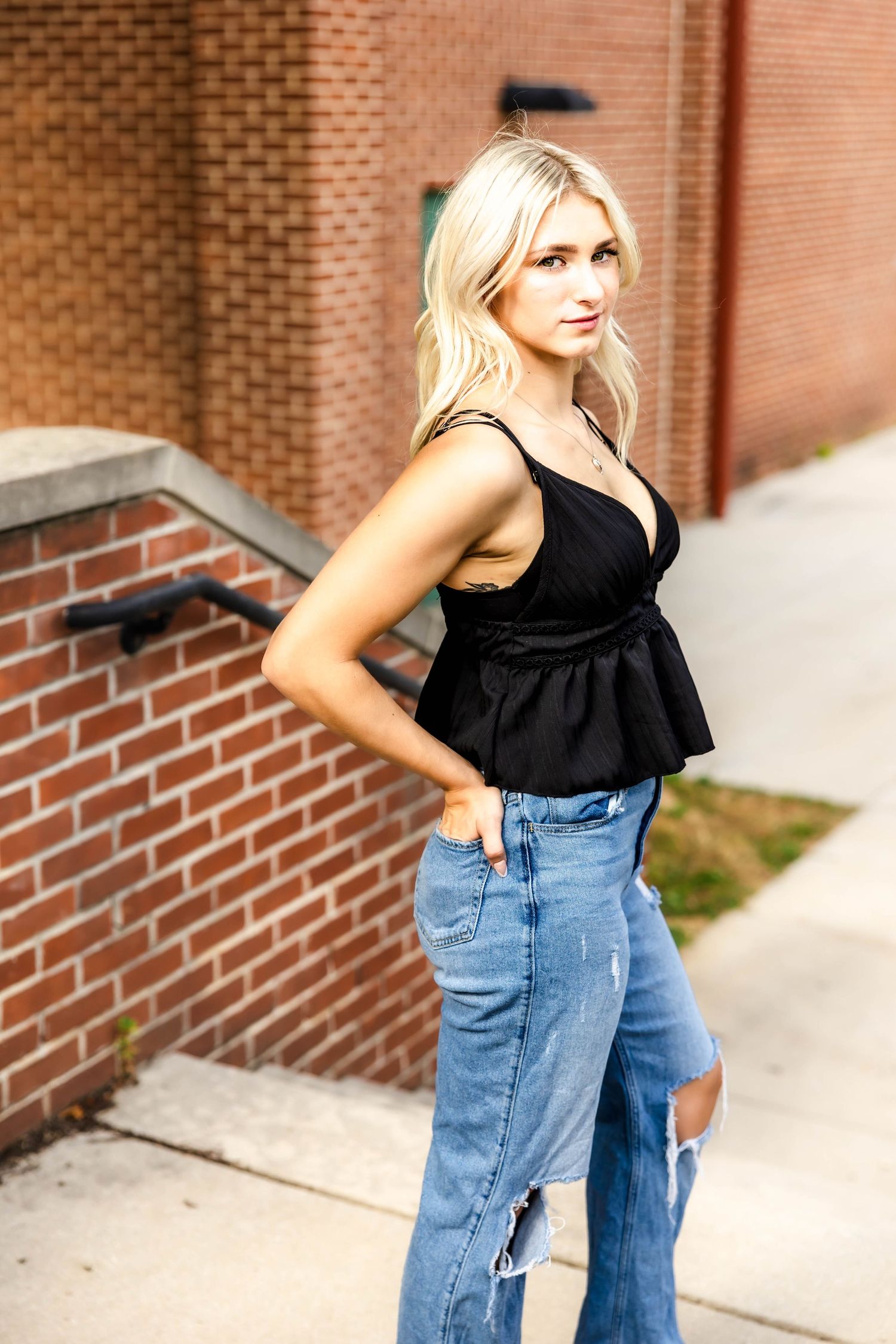 Side profile portrait showcasing black peplum top and ripped jeans against brick architecture.