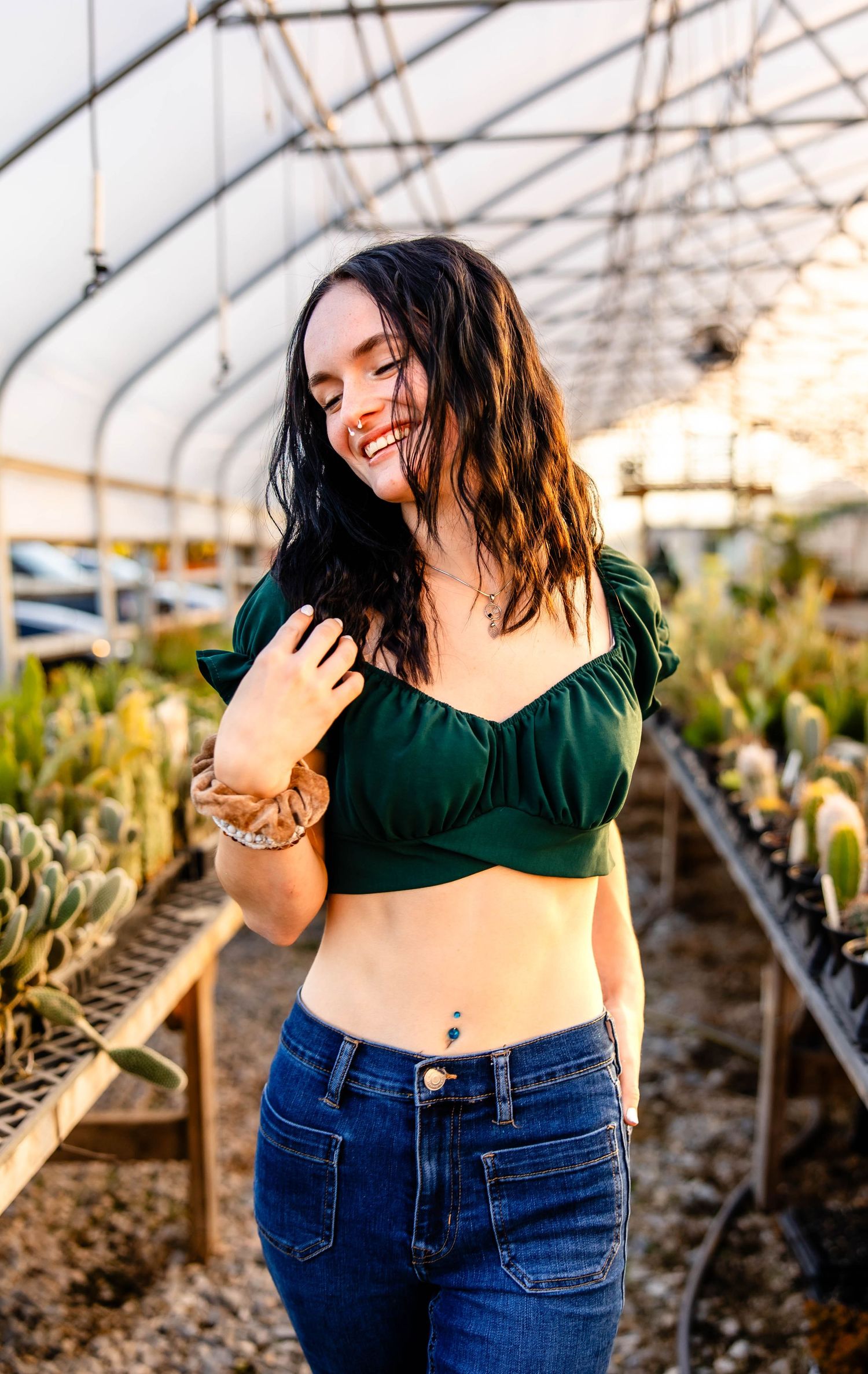 Natural light portrait in greenhouse wearing emerald green crop top and denim jeans.