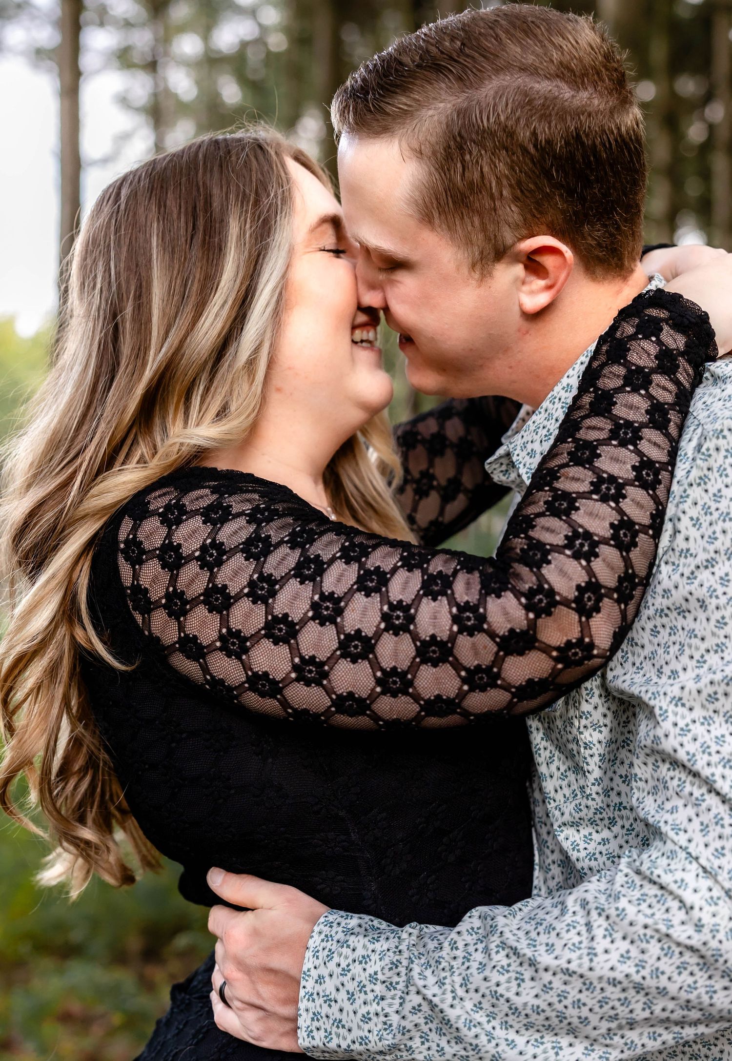 A tender moment between a couple sharing a kiss in a forest setting.