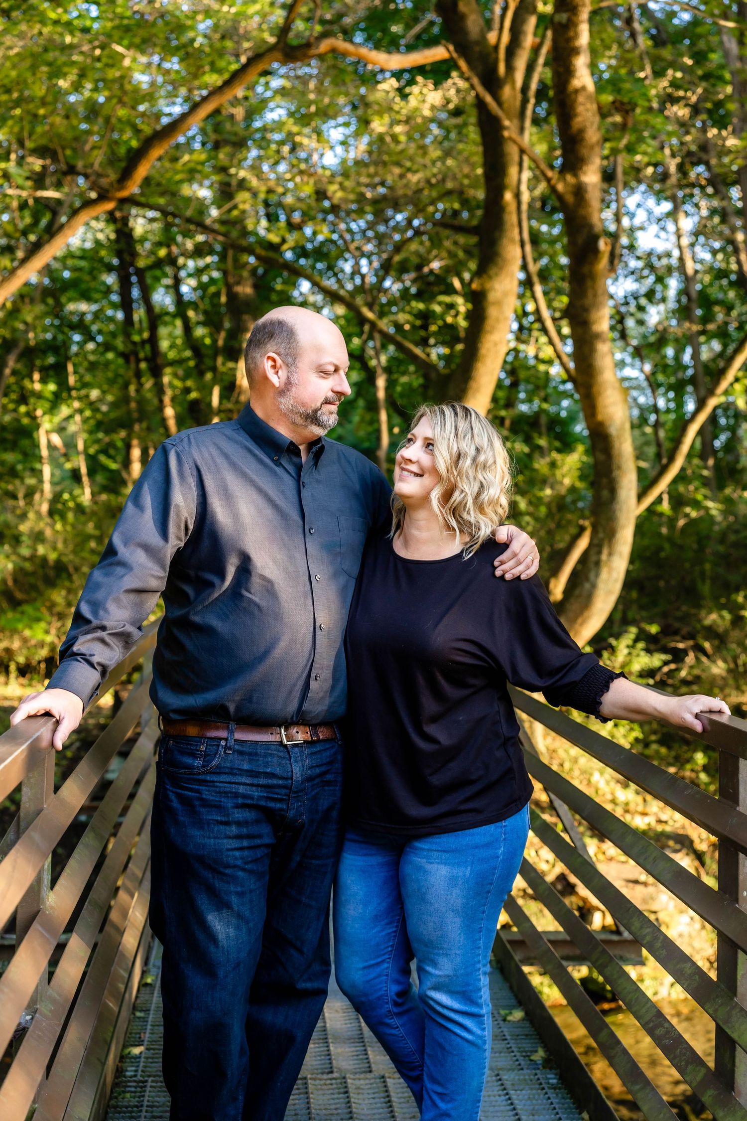 Couple sharing a candid moment on wooden bridge walkway surrounded by trees.