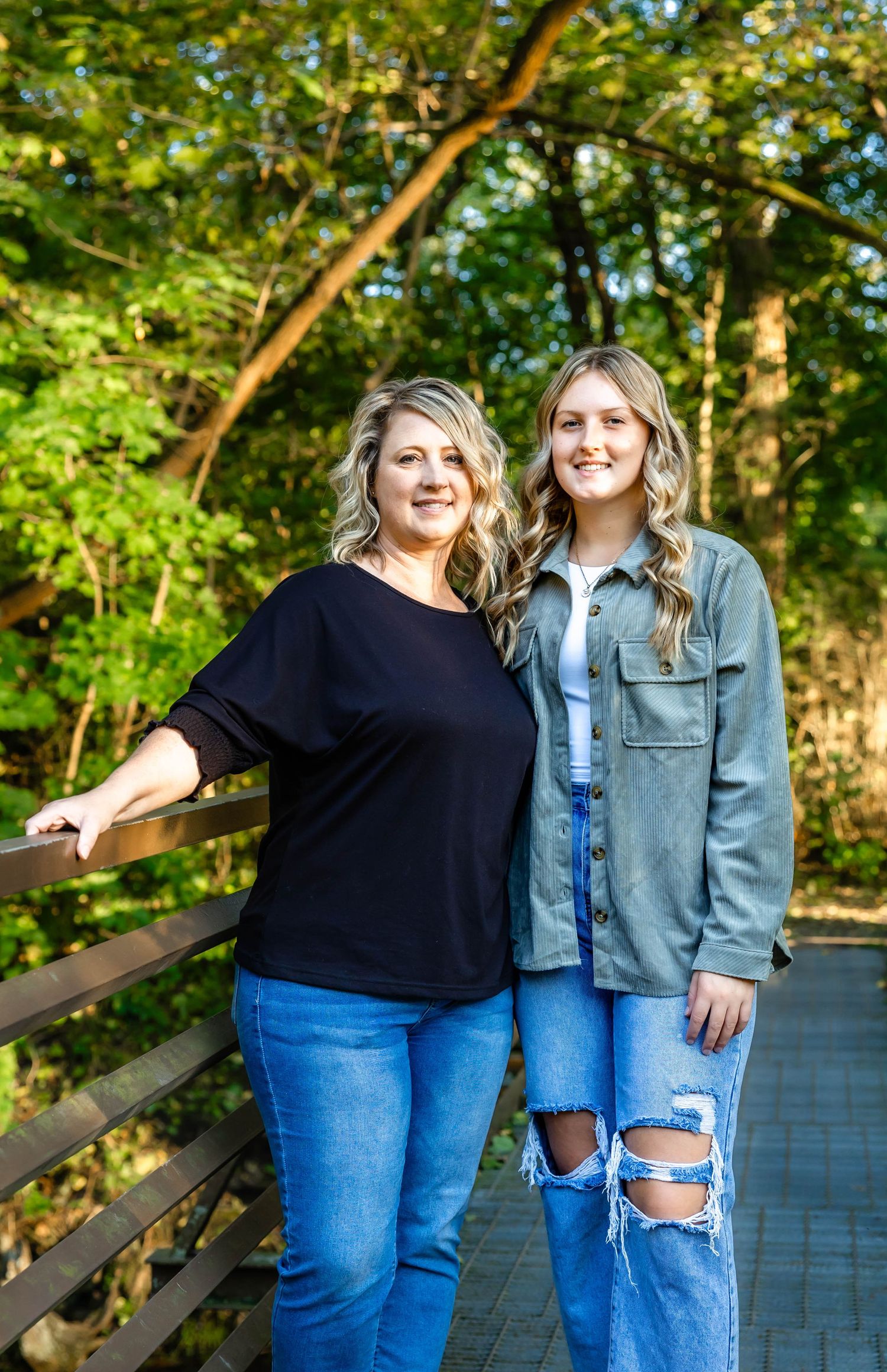 Two people in contrasting outfits stand together on sunlit wooden bridge path.