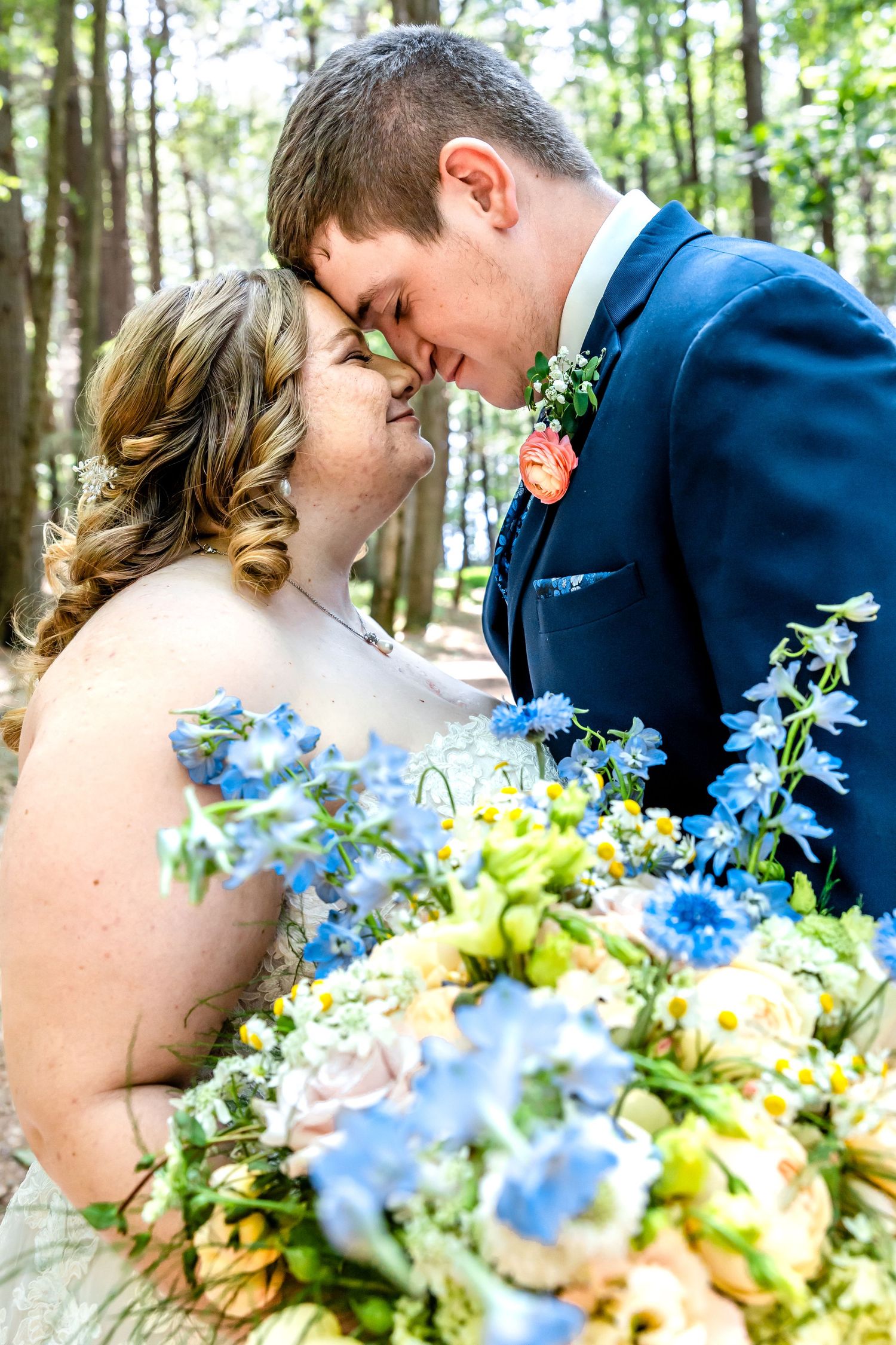 Romantic close-up of couple touching foreheads with blue and yellow flowers.