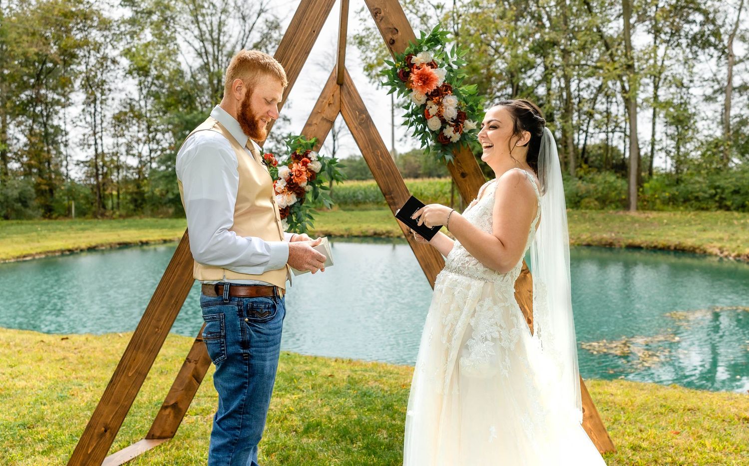 Couple reading their wedding vows in front of a wooden triangle arch at an outdoor ceremony.