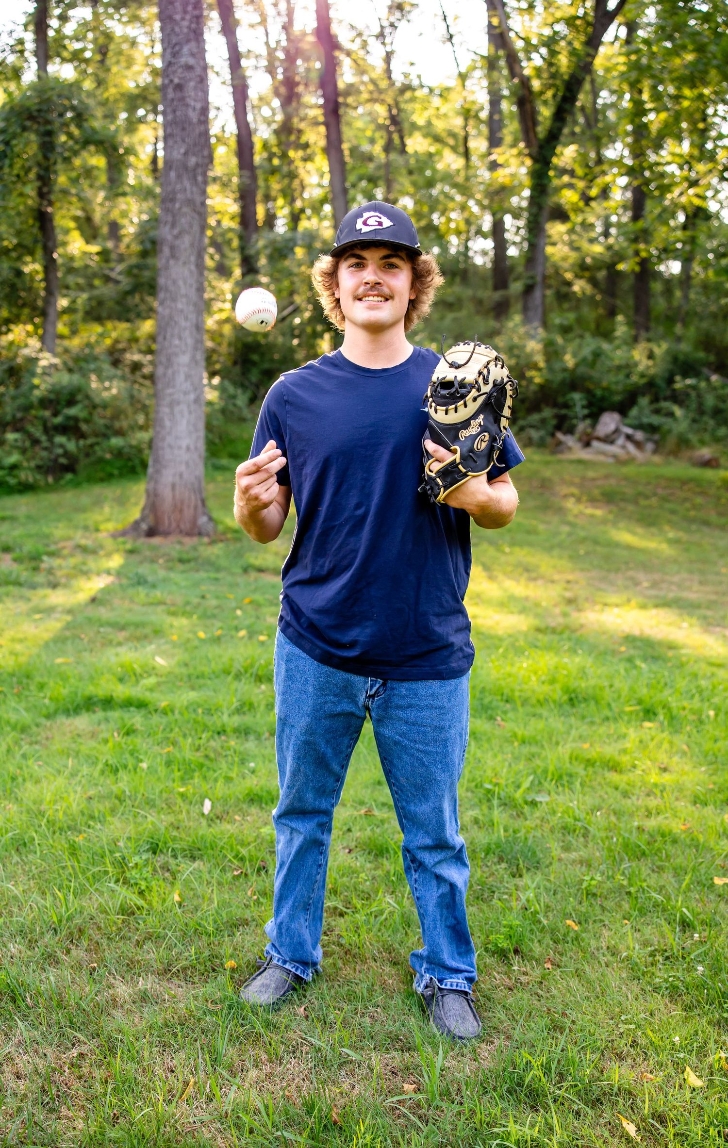 Baseball player tosses ball while holding glove in sunny outdoor setting.