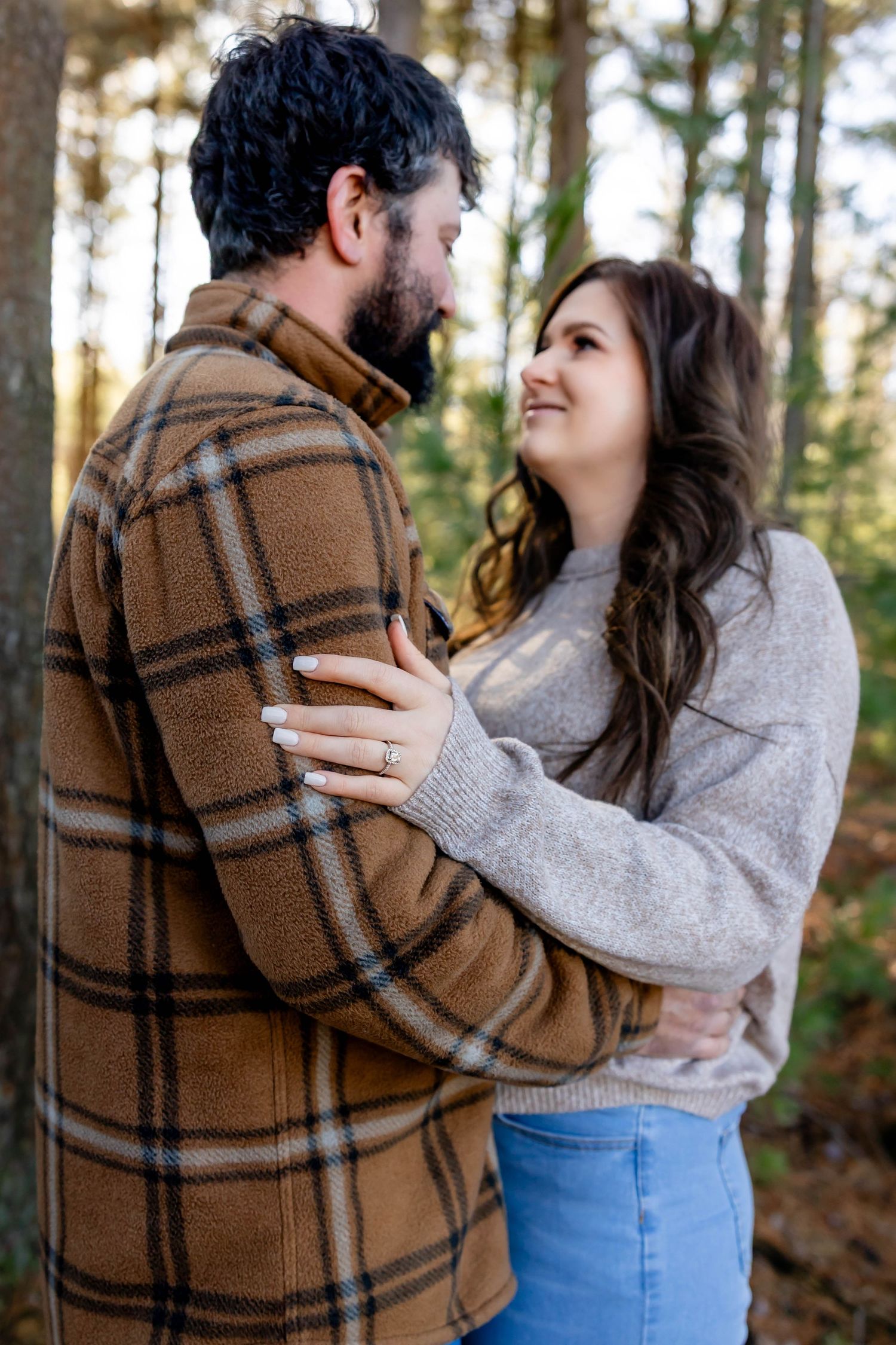 Romantic couple embracing in a wooded setting wearing casual fall clothing.