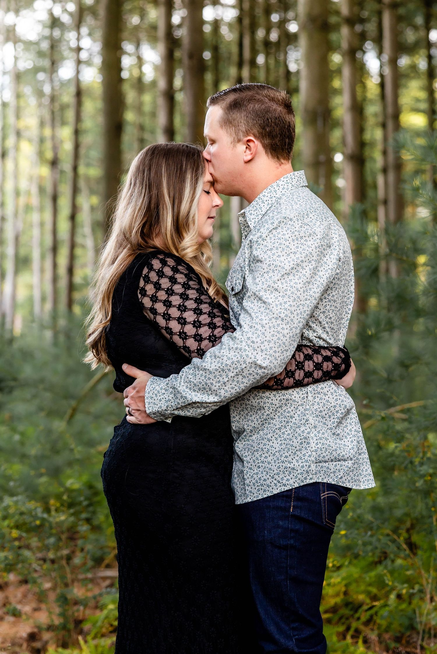 Intimate moment between couple in wooded forest setting during engagement photo session.