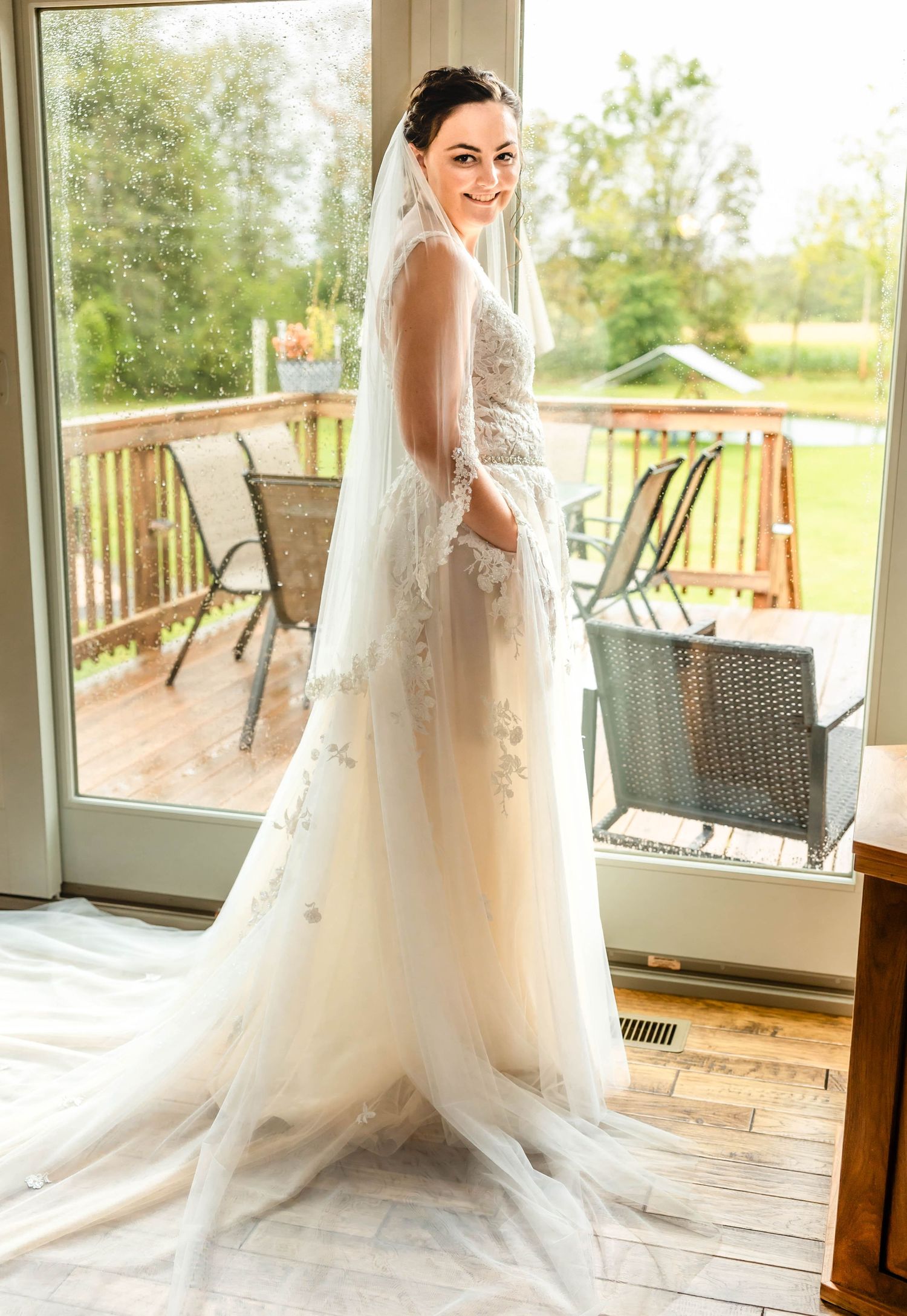 Elegant bridal portrait showcasing flowing lace dress against sunlit window backdrop.
