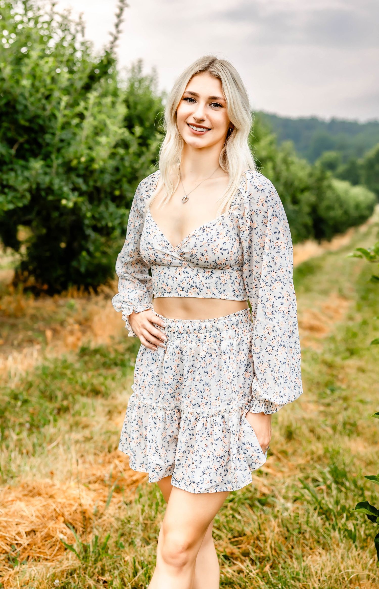 A floral two-piece dress ensemble photographed in a scenic outdoor orchard setting.