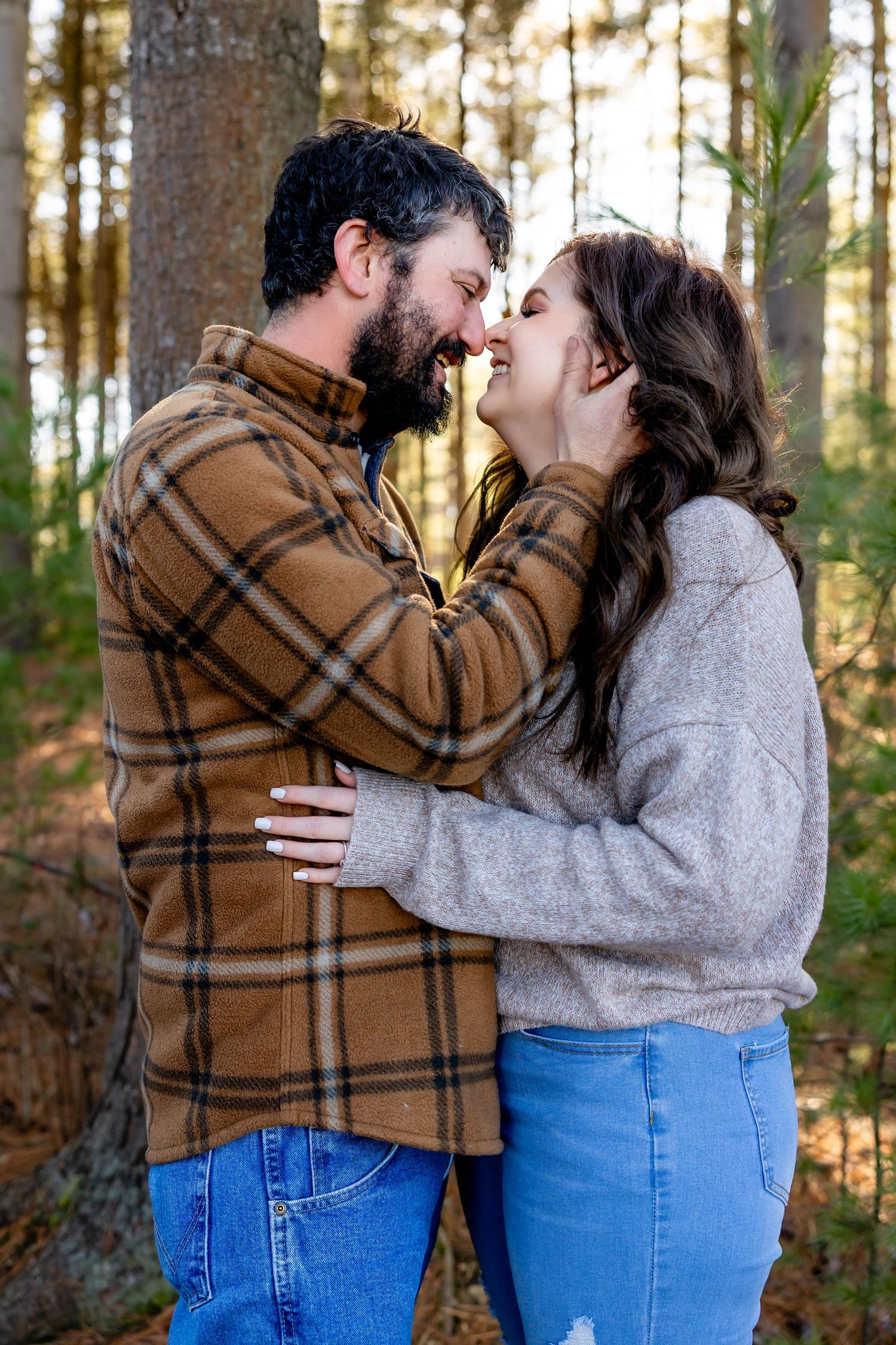 Couple sharing intimate kiss in sunlit forest wearing casual attire.