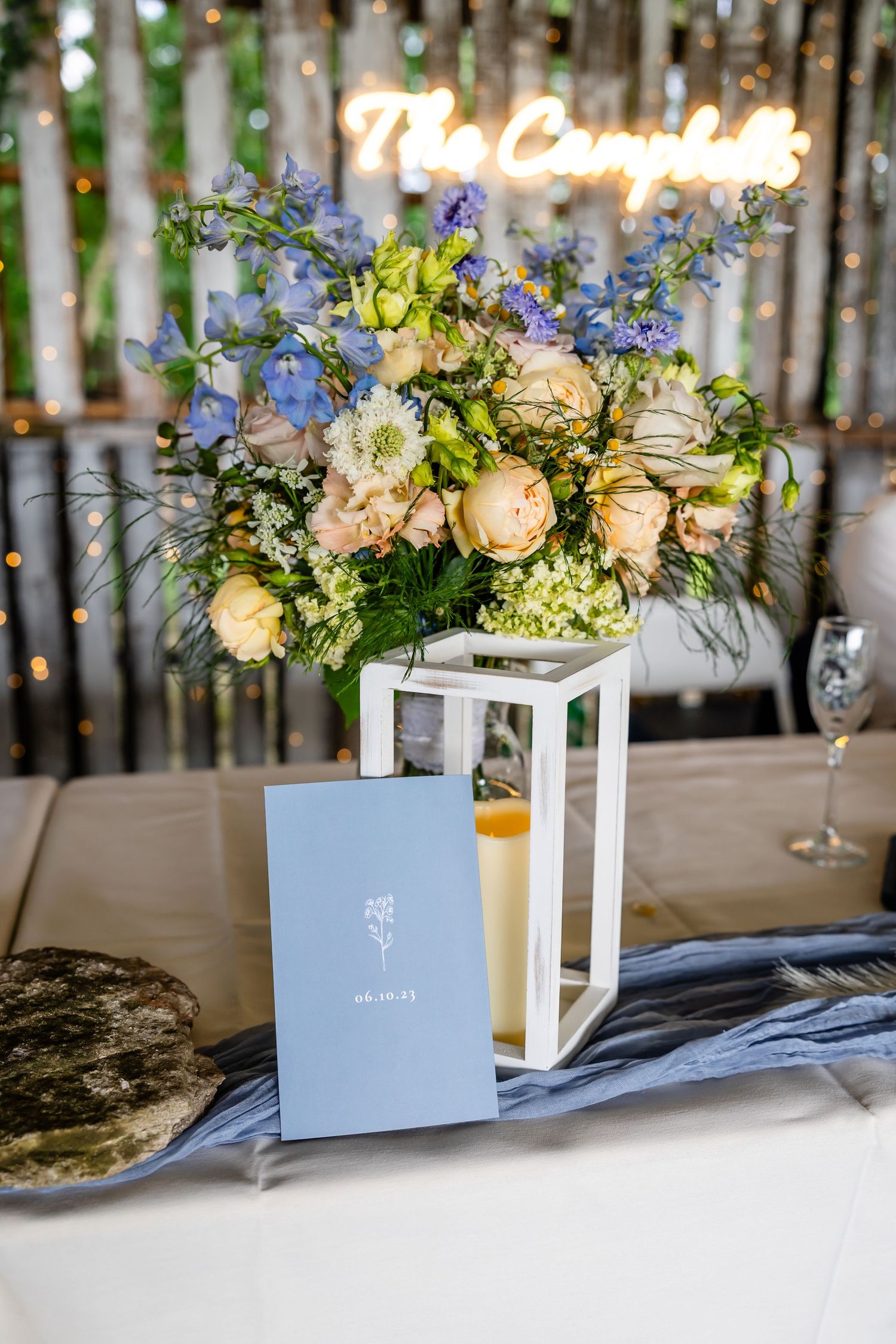 Elegant table setting with floral centerpiece, lantern and menu card beneath glowing neon signage.