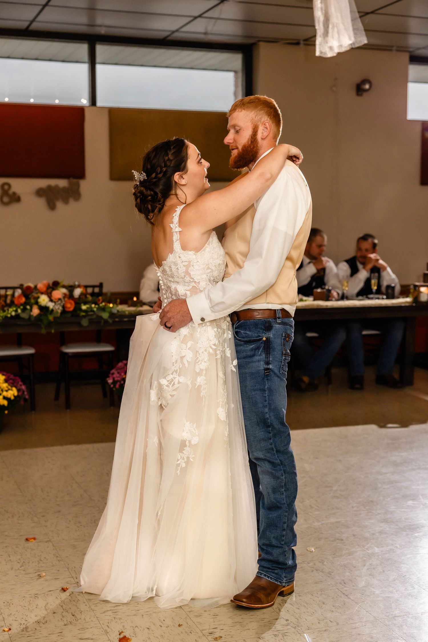 A couple shares their first dance at a rustic wedding reception venue with string lights overhead.