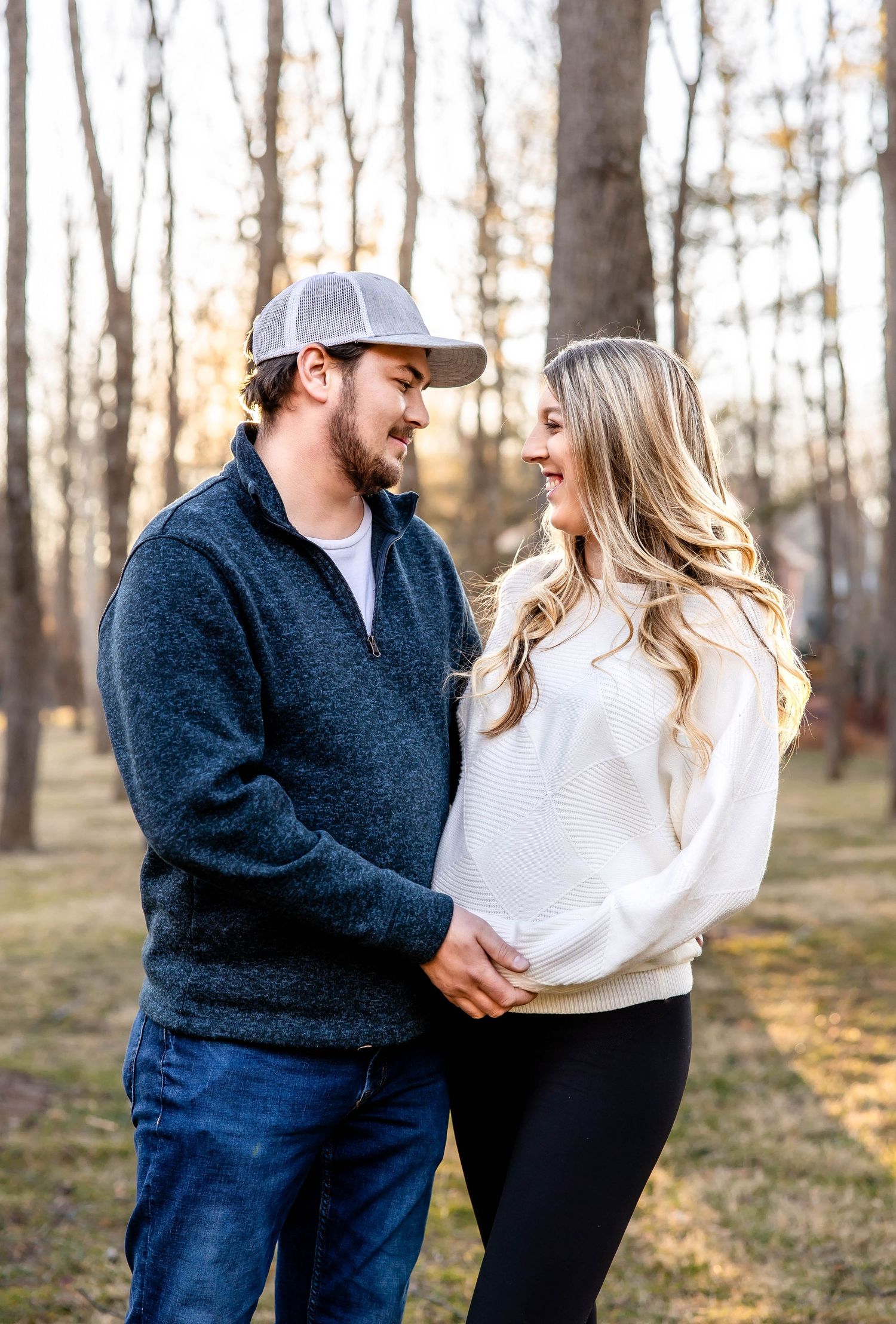 Couple in casual autumn outfits sharing an intimate moment among bare trees in a wooded setting.