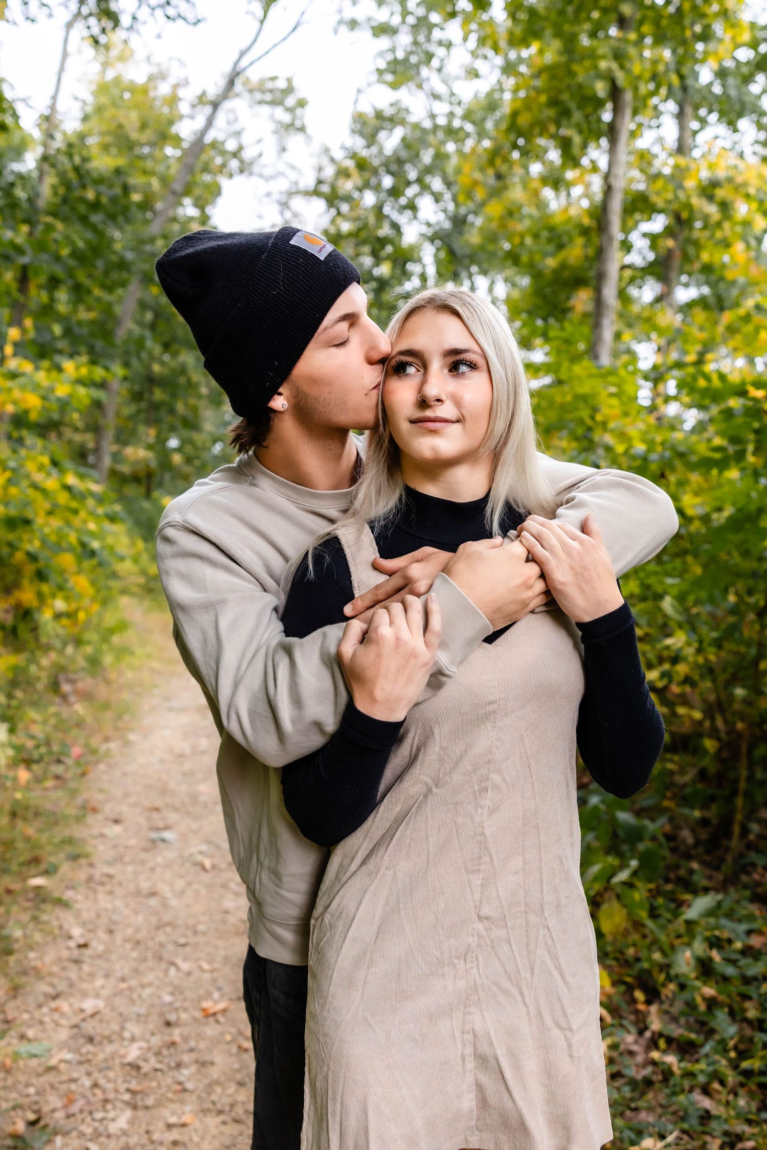 A sweet embrace between a couple on a wooded path during fall.