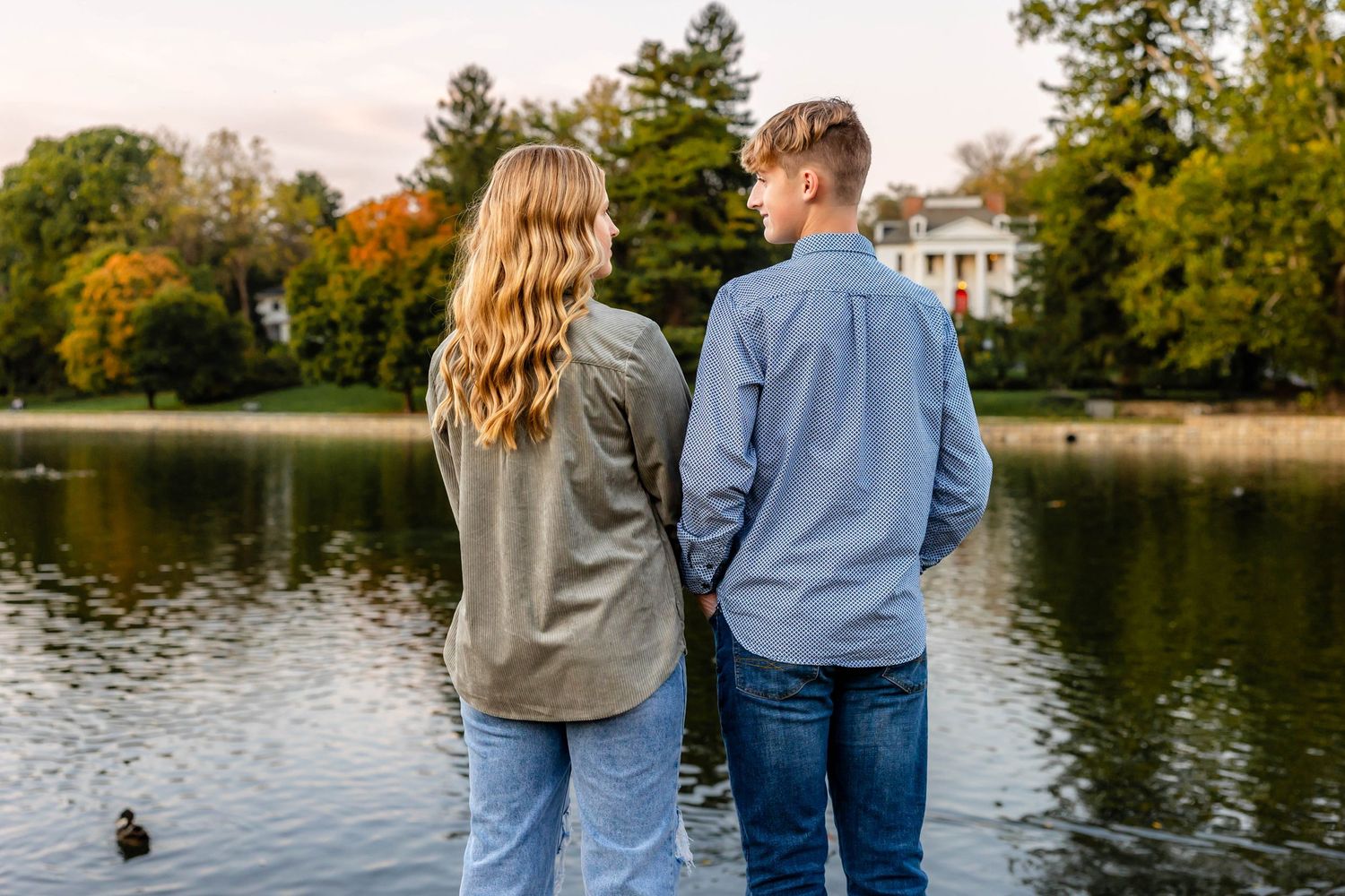 Back view of couple watching ducks swim on a peaceful autumn lake.
