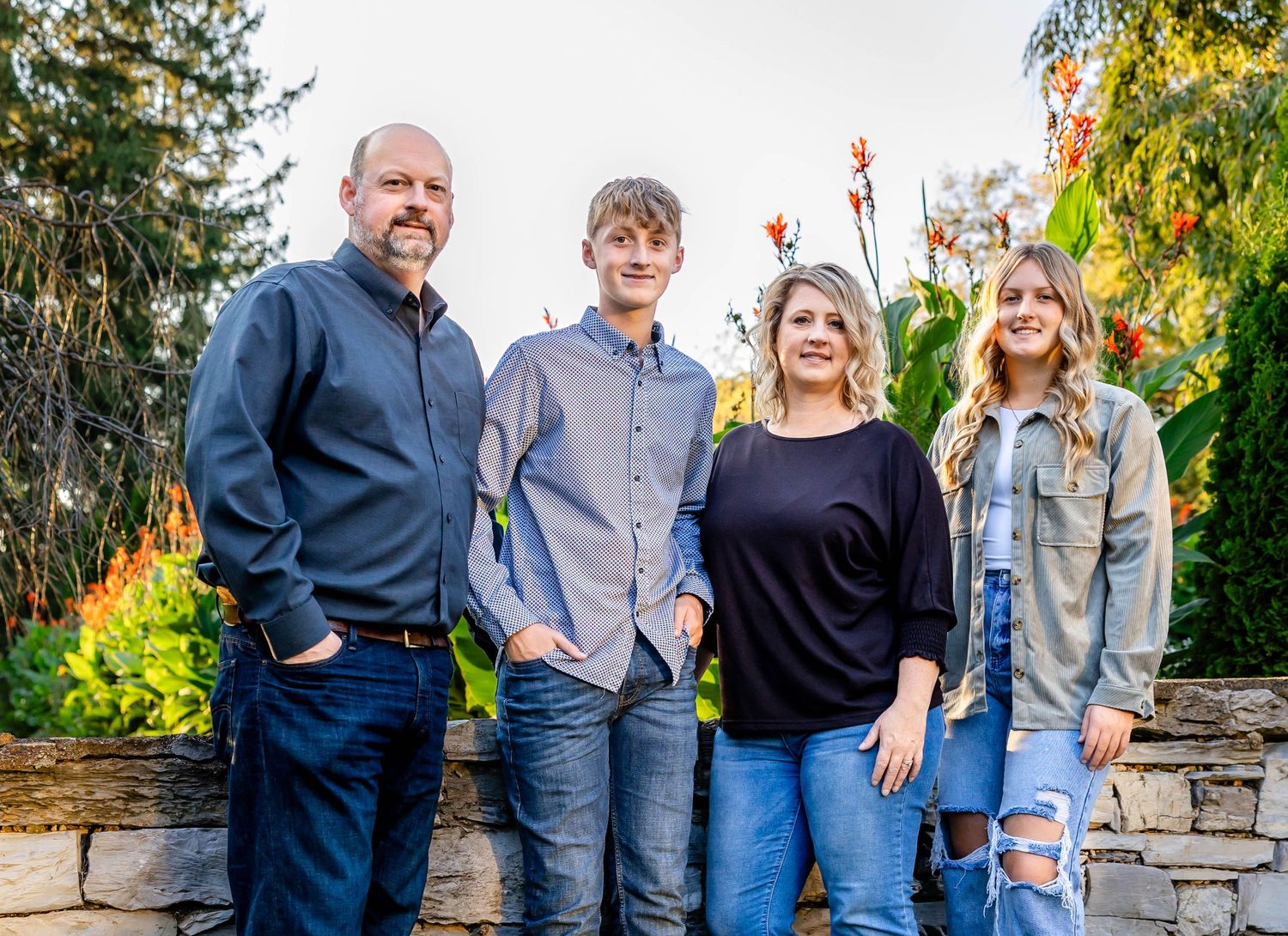 A family group poses together in front of autumn foliage and a decorative stone wall.