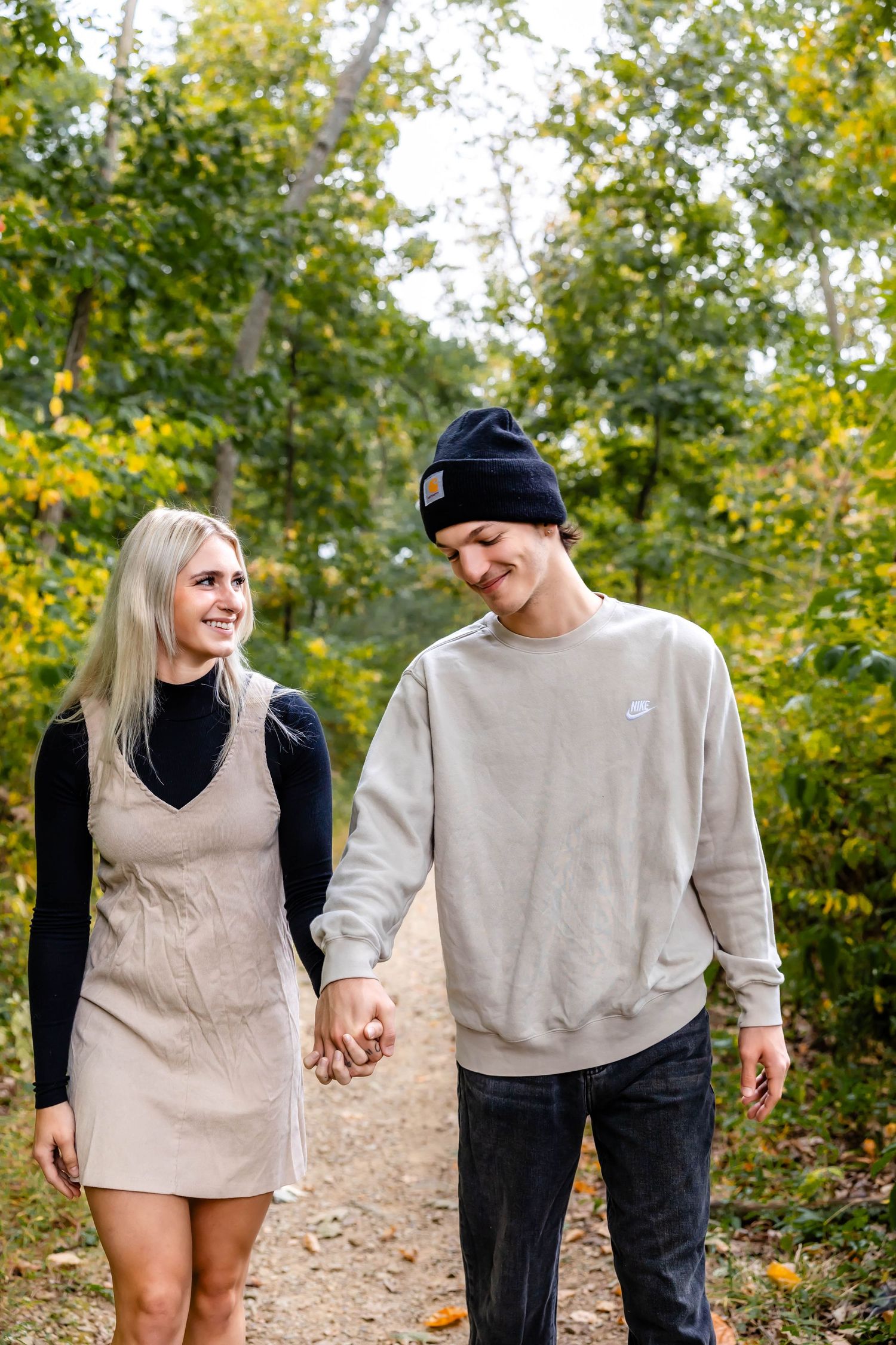 A laughing couple takes a stroll together on a dirt path surrounded by yellow and green trees.