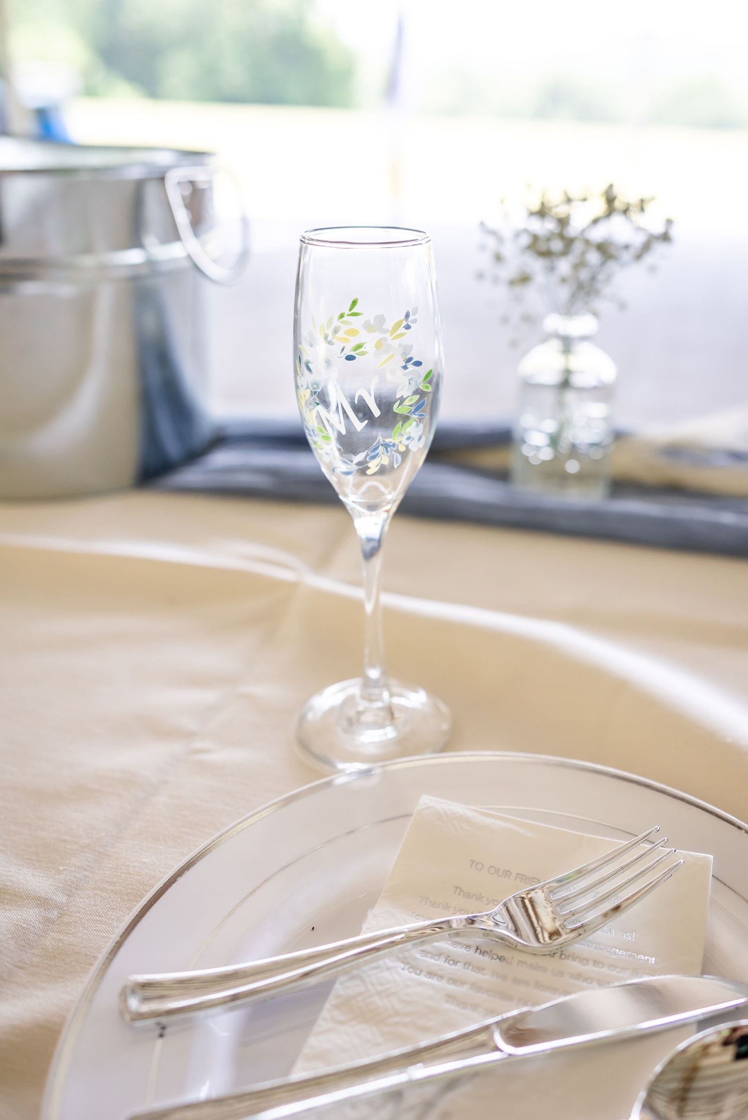 Elegant place setting with champagne flute, white plate, and silverware on cream tablecloth.