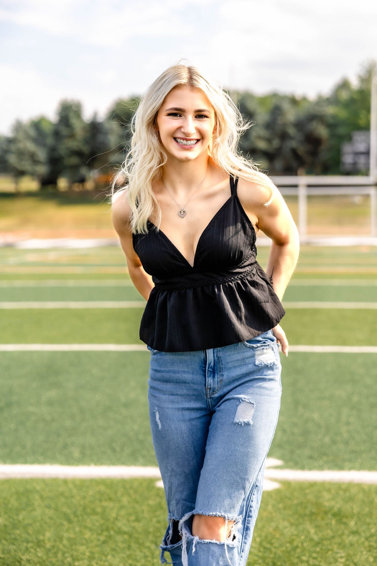 Summer fashion portrait on sports field in black peplum top and distressed jeans.