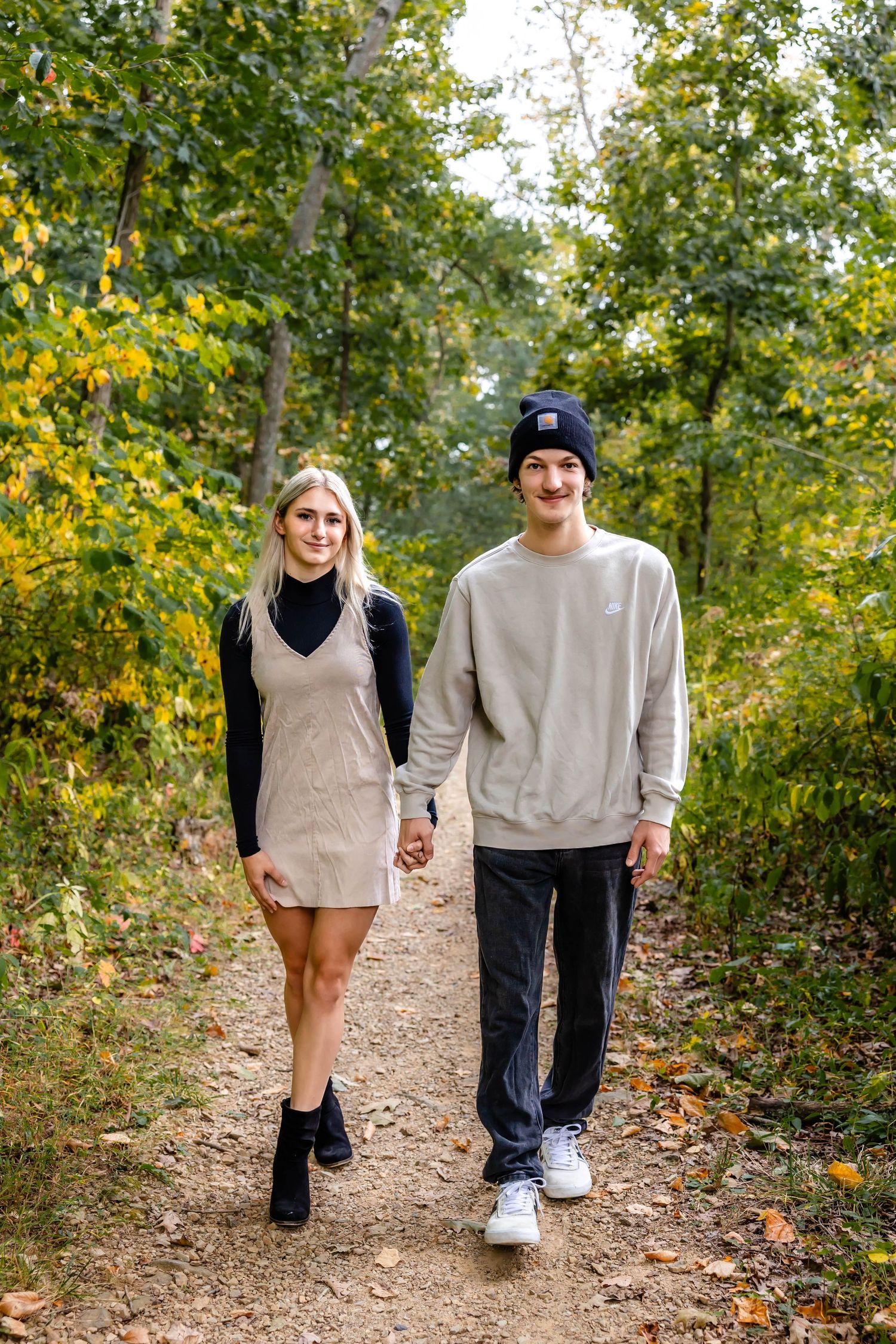 A couple walks hand in hand down a scenic autumn trail surrounded by golden foliage.