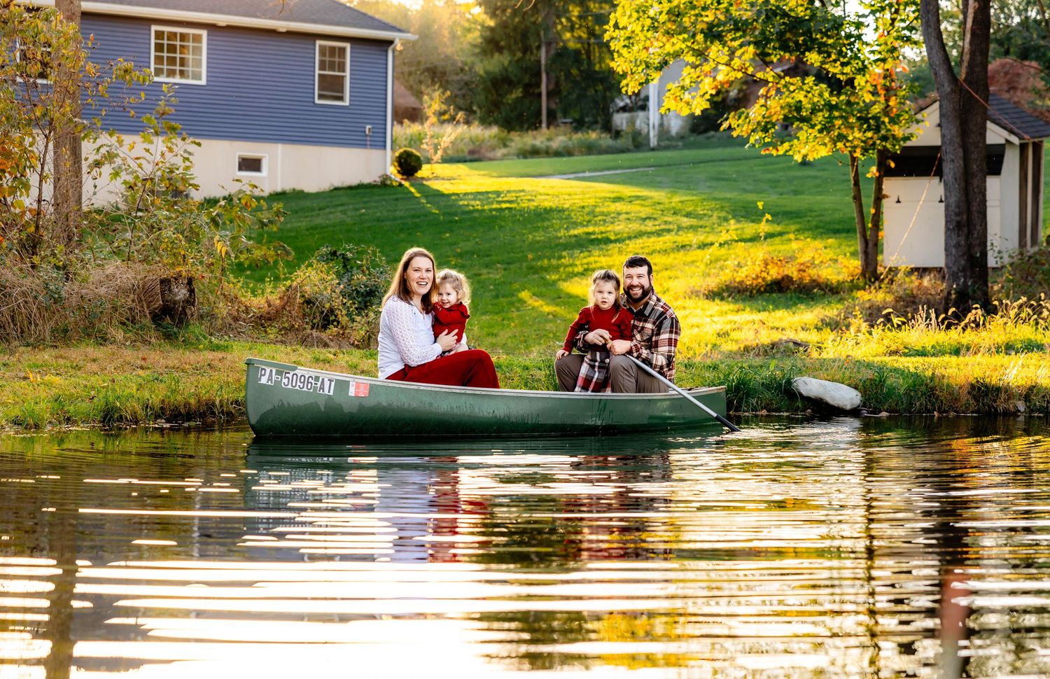 A group enjoys an autumn afternoon in a canoe on a peaceful pond next to a blue house.