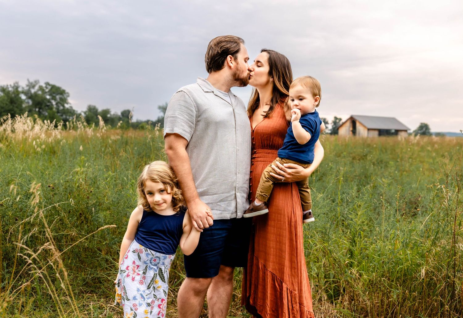 A family shares a tender moment together in a grassy field at sunset wearing coordinated casual outfits.