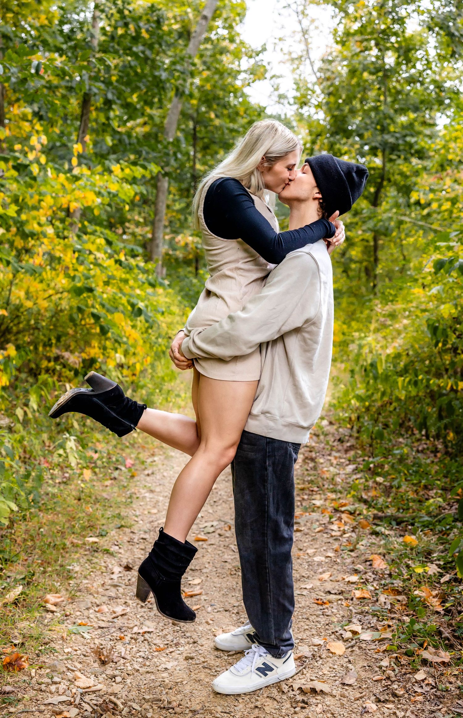 Playful couple sharing romantic moment on forest trail during autumn photoshoot.
