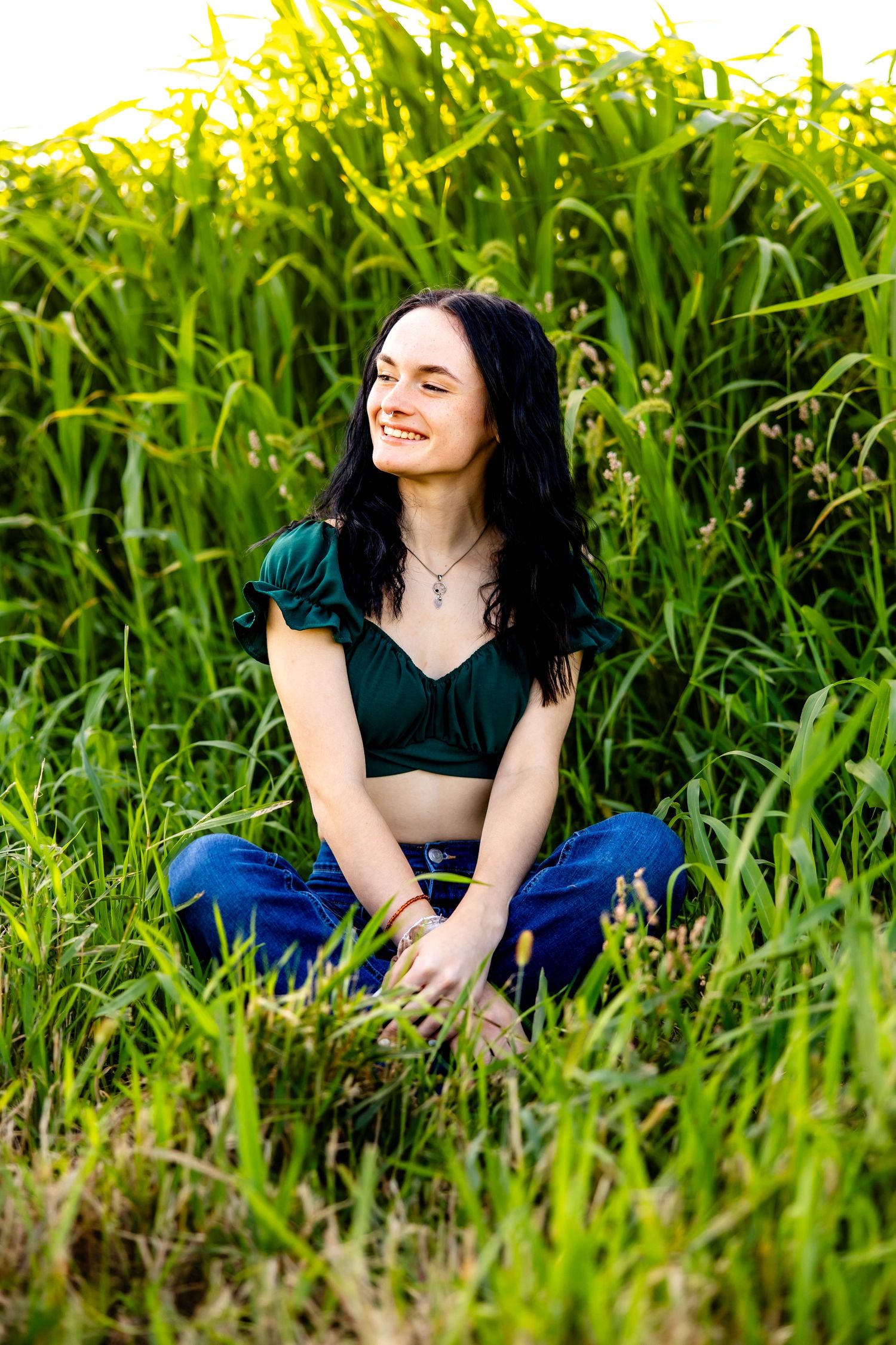 A joyful outdoor portrait in a cornfield featuring a green crop top and blue jeans on a sunny day.