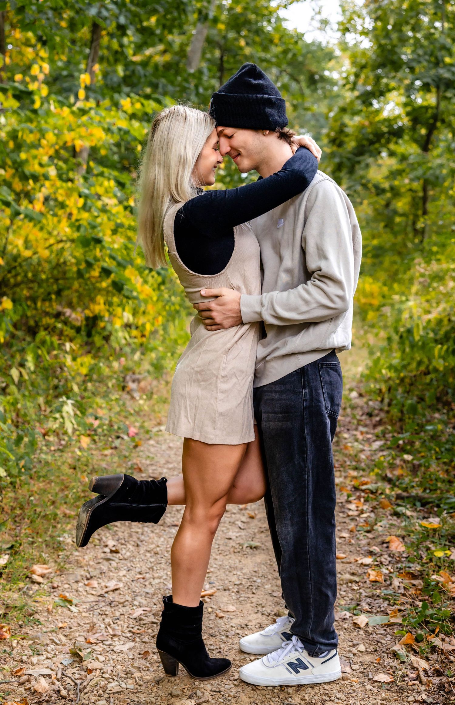 A romantic couple shares an intimate moment on a wooded trail in autumn.