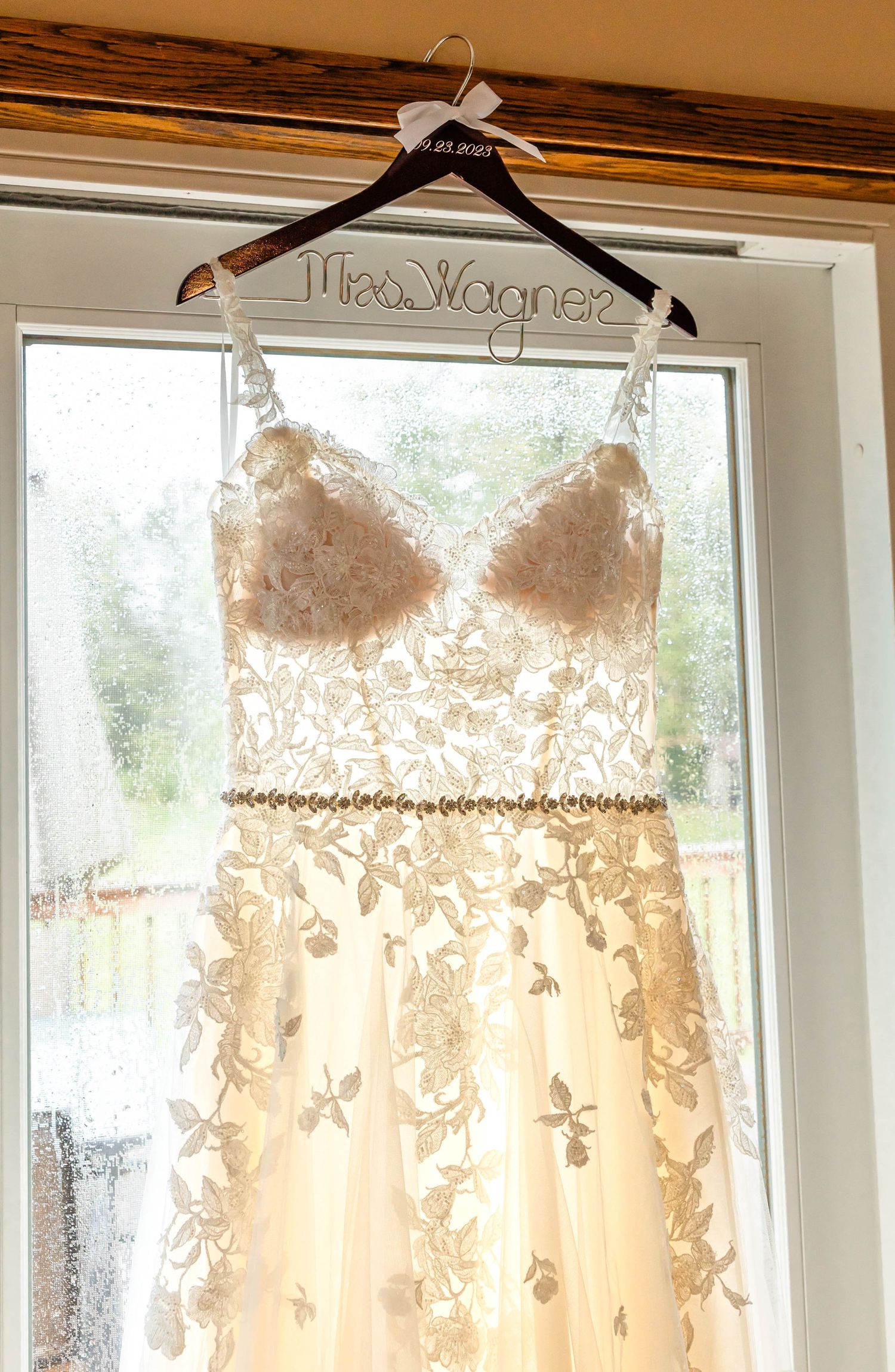 Close-up of detailed lace wedding gown with personalized hanger displayed in window.