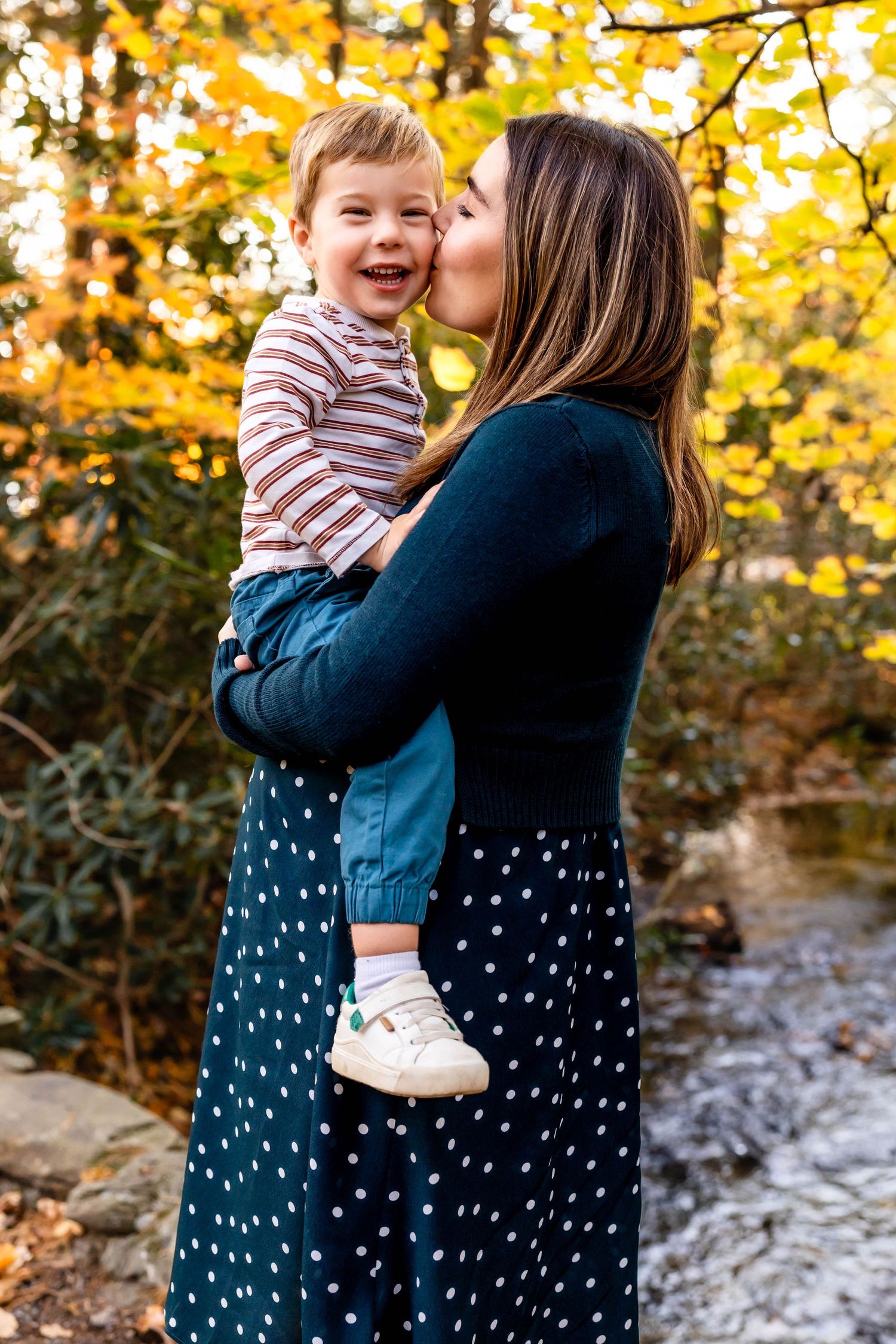 A parent and child share a tender moment surrounded by golden autumn foliage.