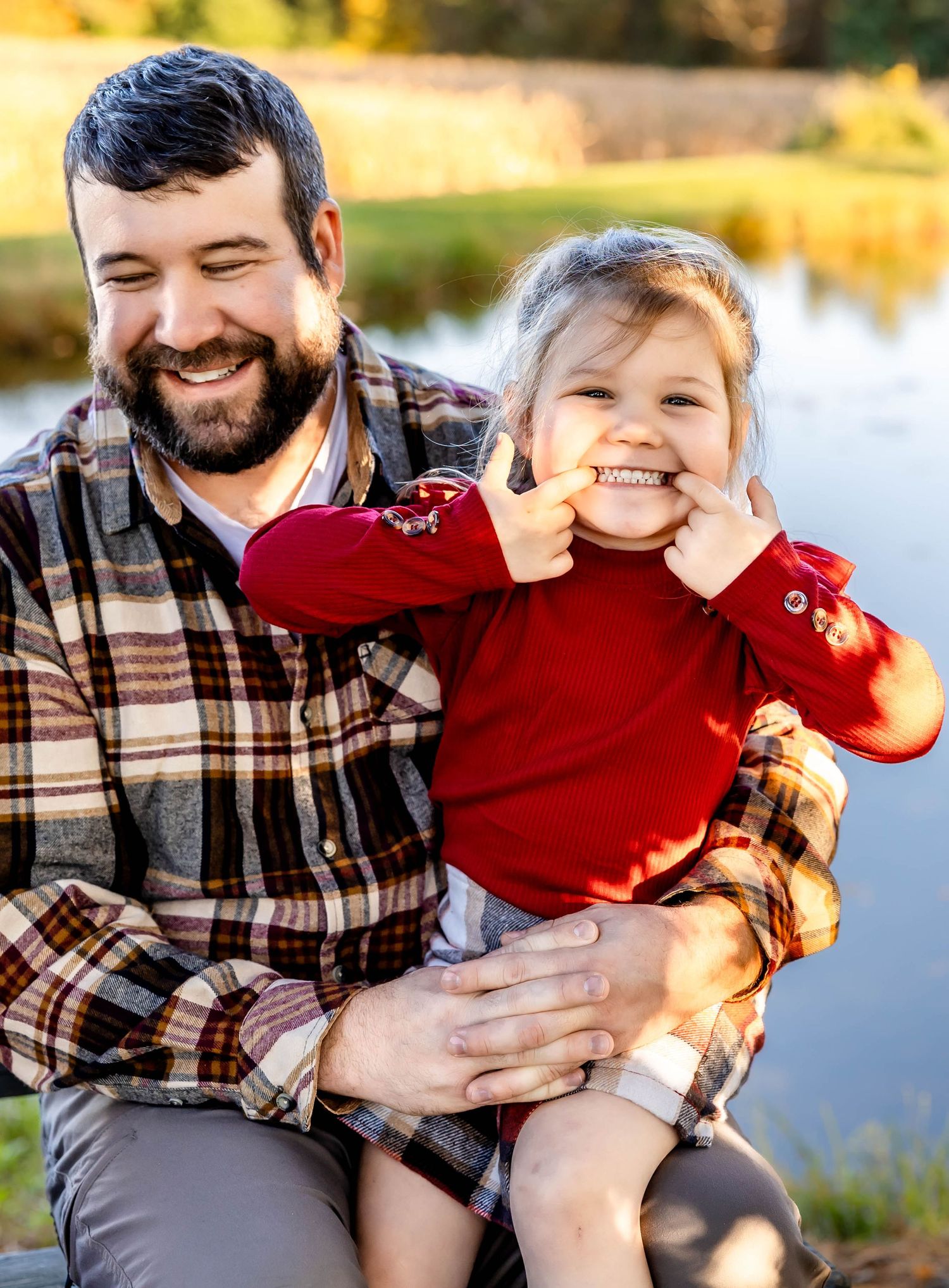Playful moment between parent and child in red sweater by lakeside.