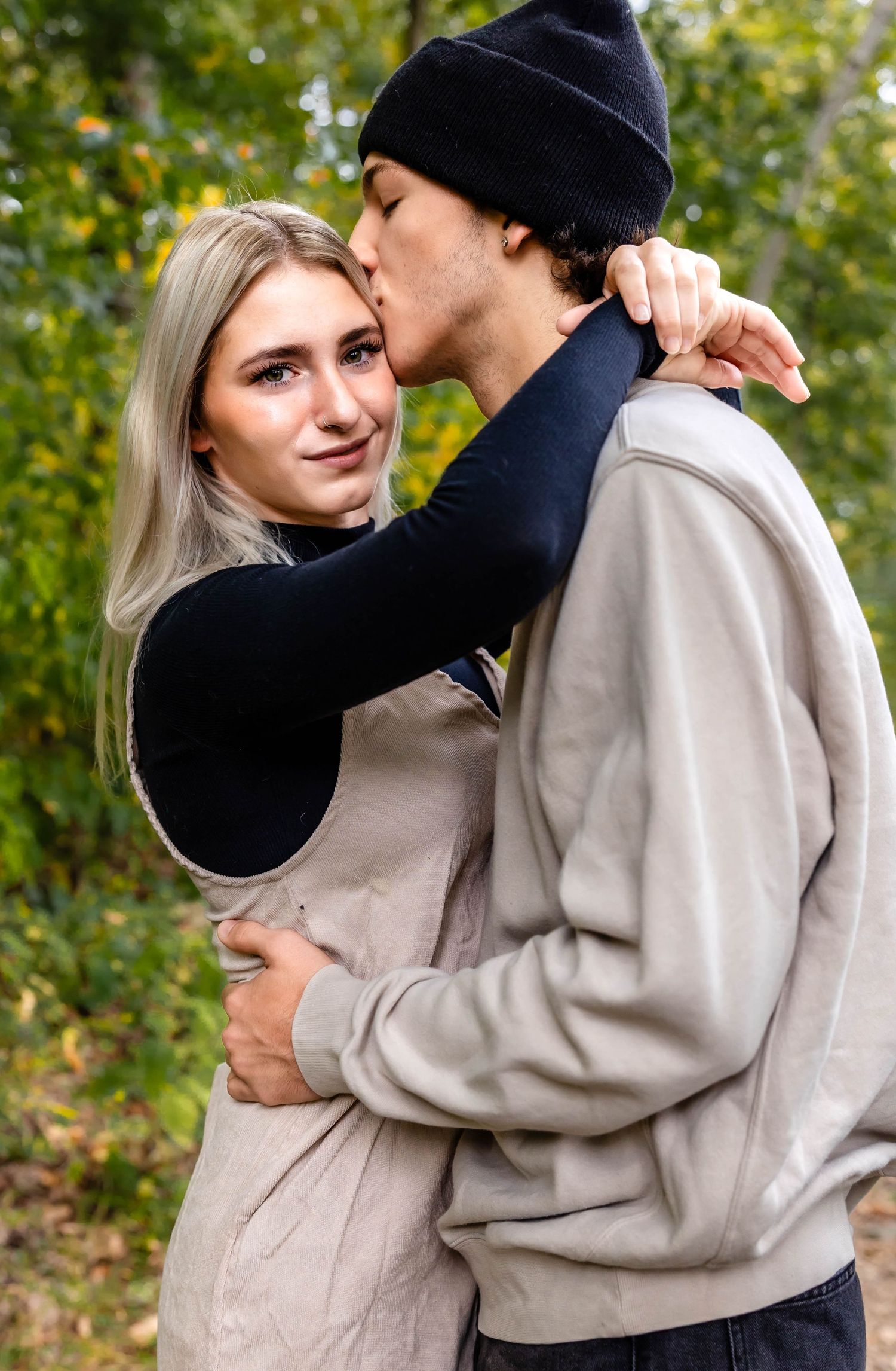 An affectionate couple embraces outdoors with fall foliage creating a romantic backdrop.