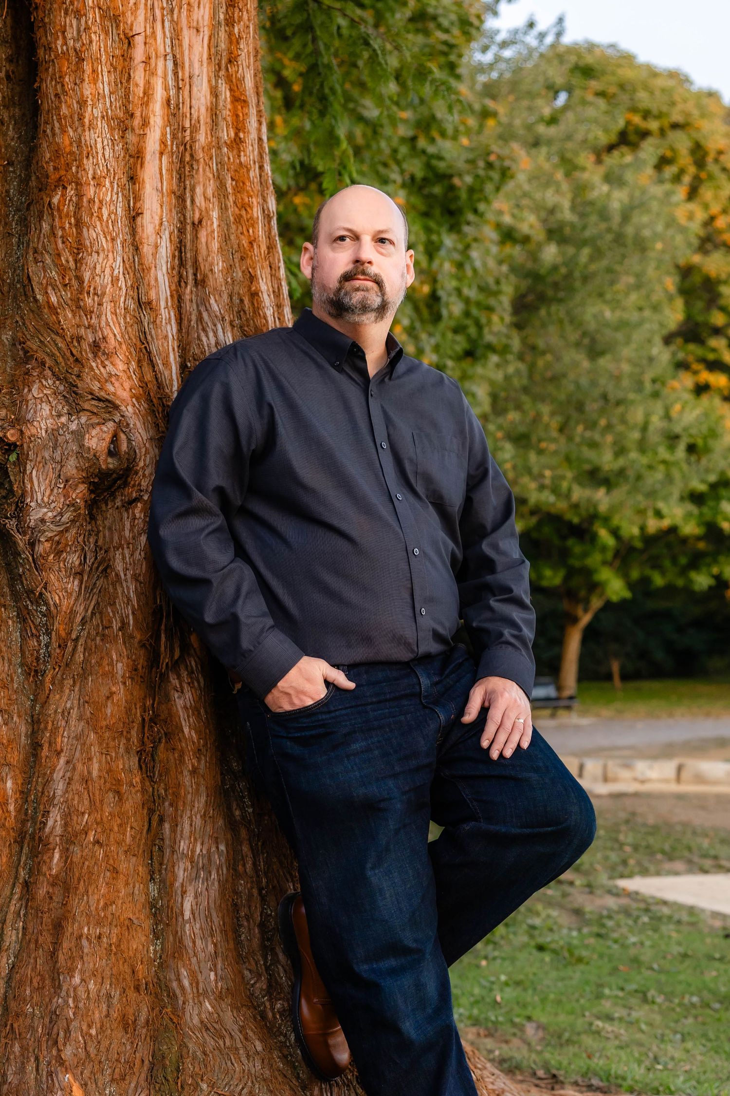 Portrait against tree featuring person in navy jacket and dark jeans in outdoor setting.