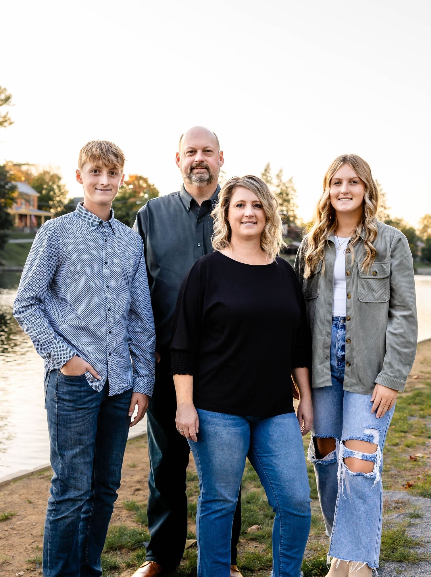 Family portrait with four members standing together outdoors in coordinated blue and black outfits.