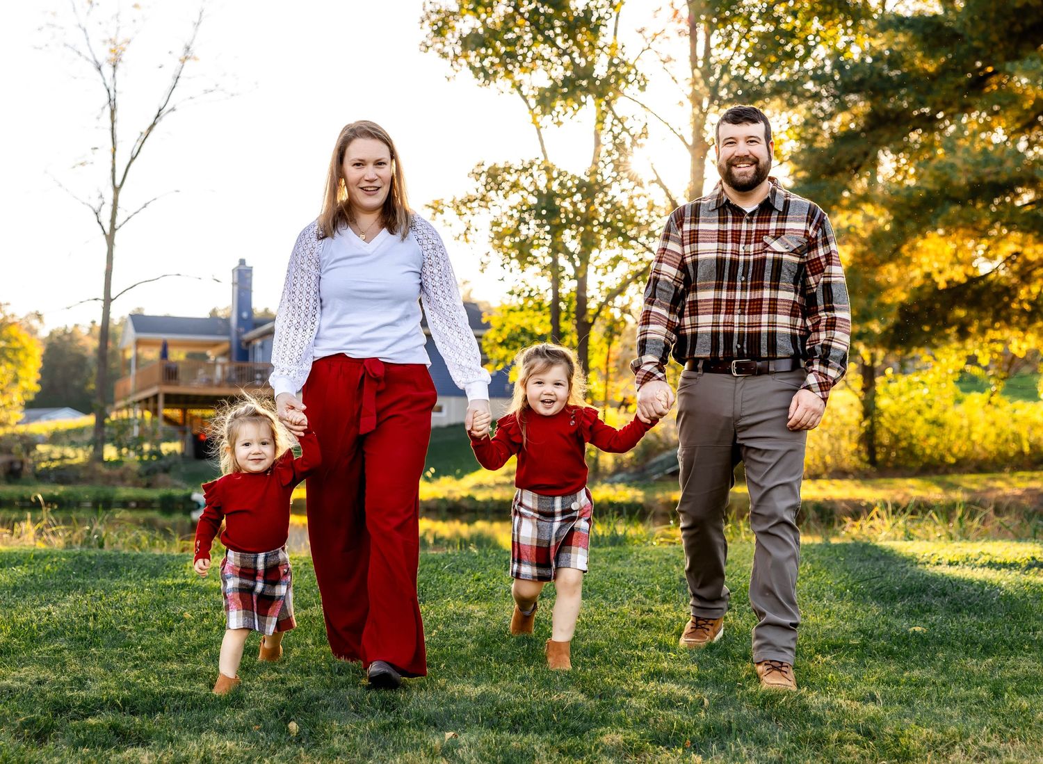 A family holds hands while walking through a sunlit park with fall foliage.